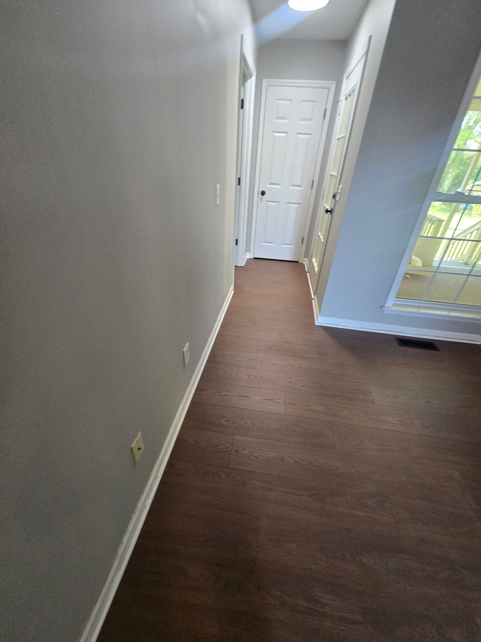 Empty hallway with beige walls, brown carpet, and a white door at the end near a window.