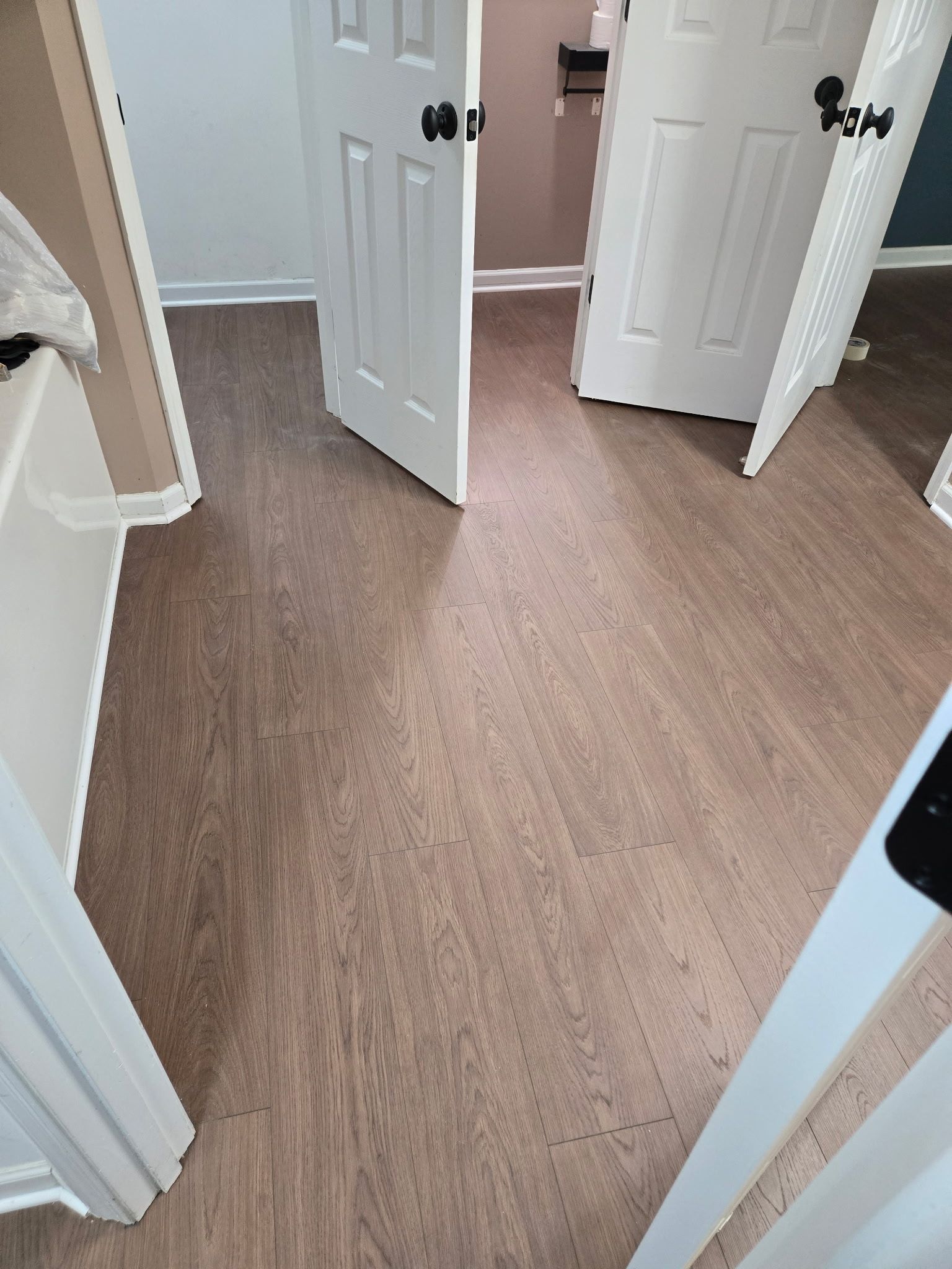 Hallway with wood-look floor and open white doors, viewed from an entryway.