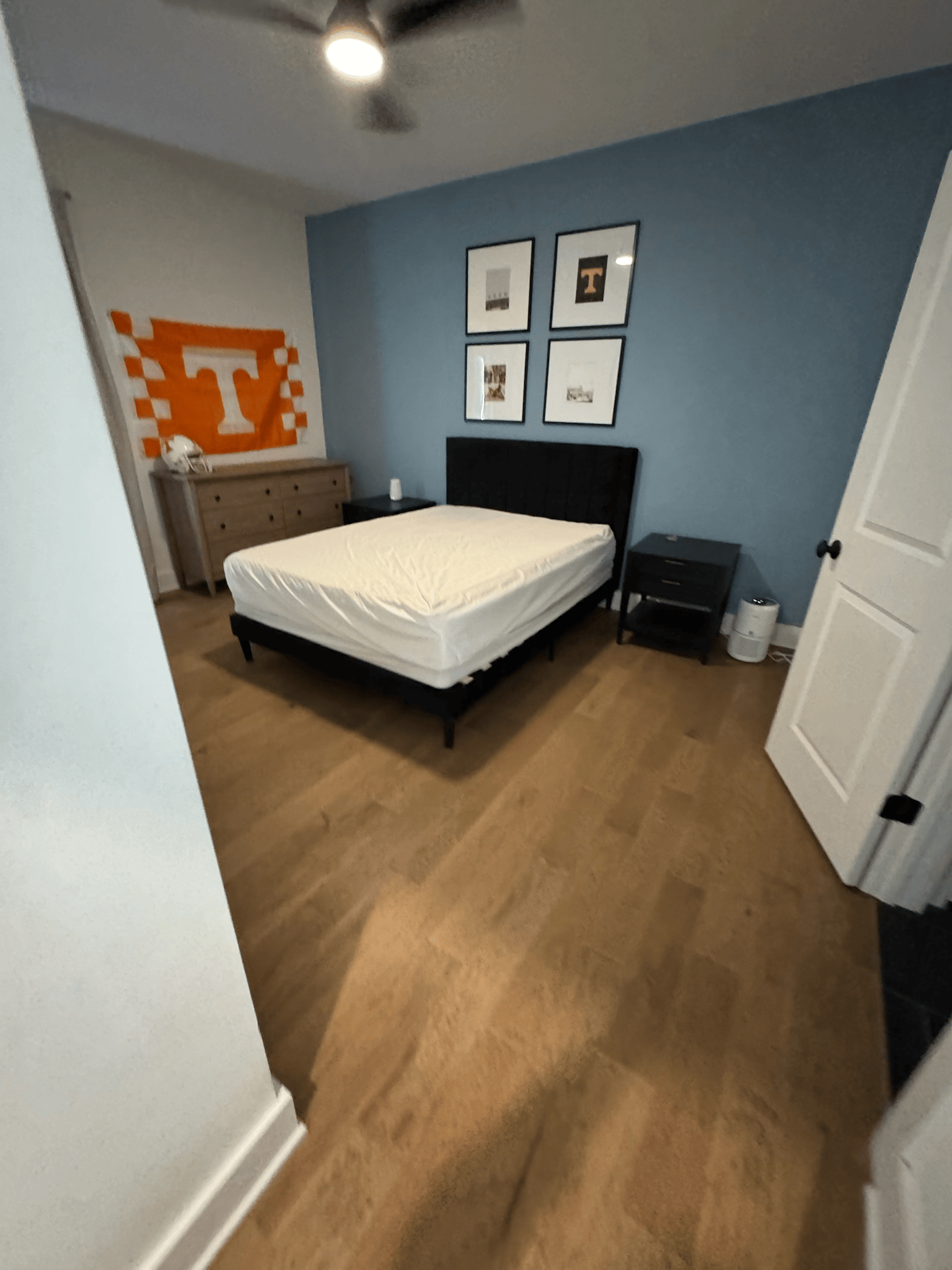 Small bedroom with a bed, dresser, blue wall, and orange sports decor.