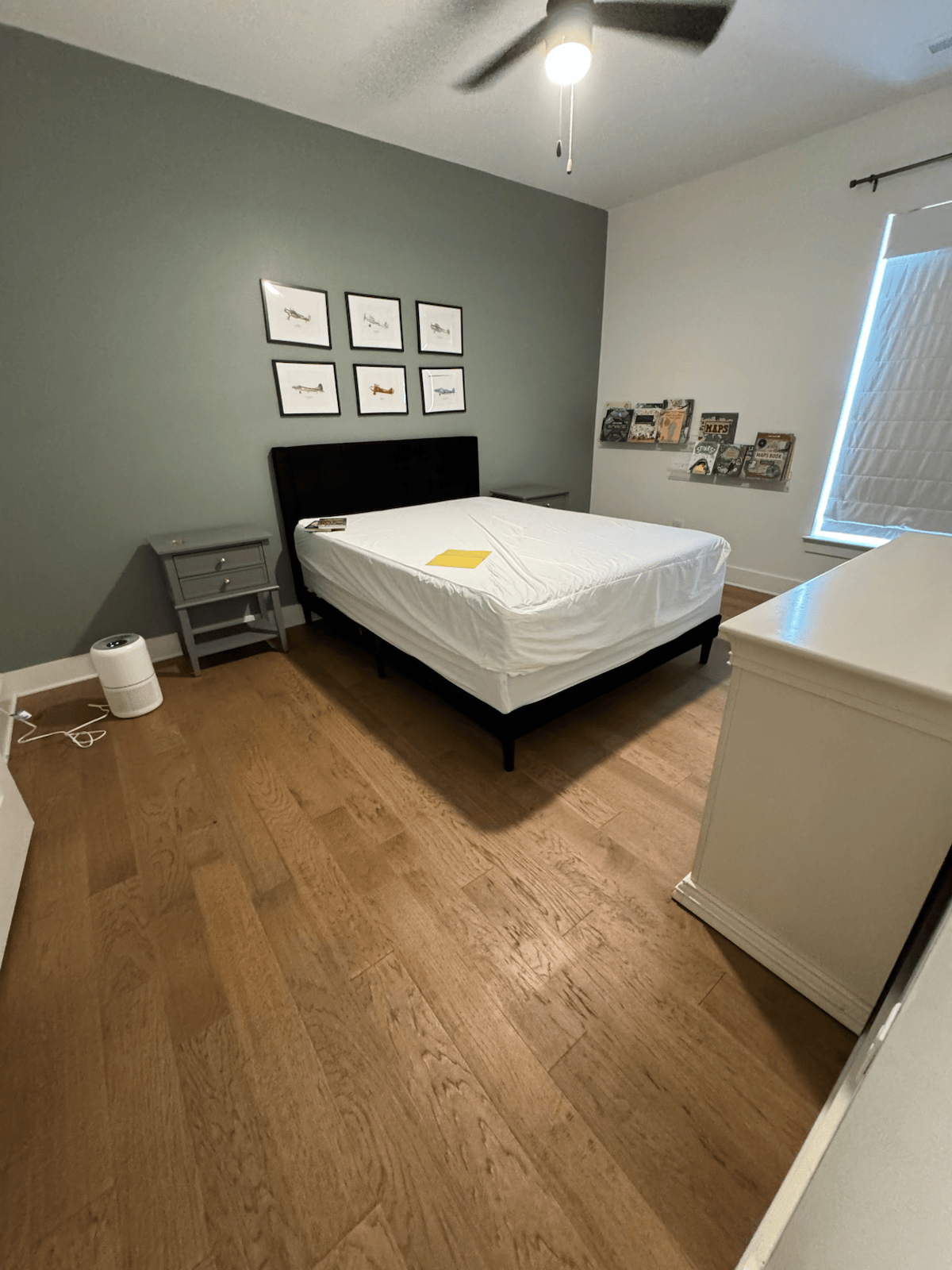 Minimal bedroom with a black bed, gray walls, wood floor, white dresser, and framed art above the headboard