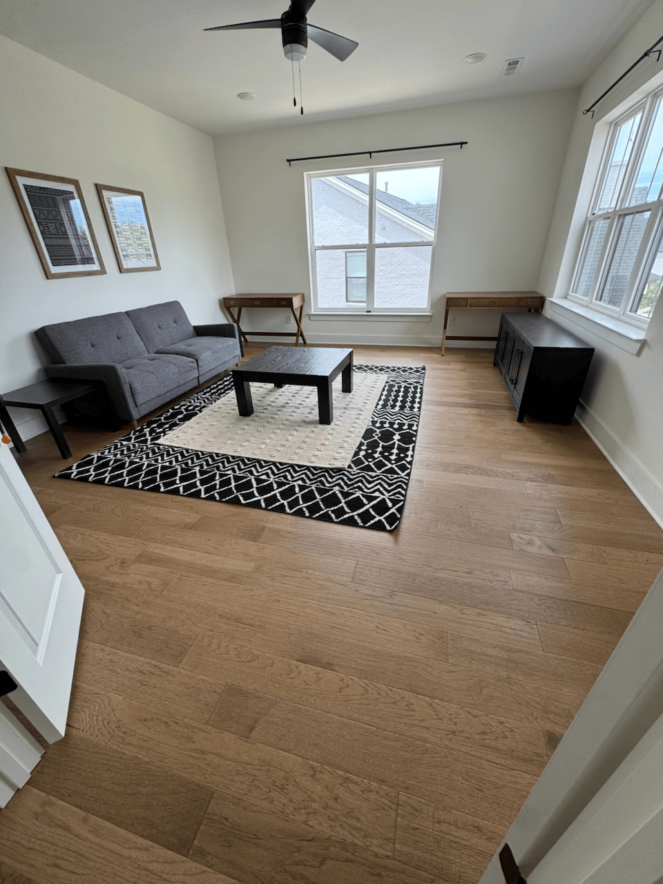 Empty living room with gray sofa, black coffee table, patterned rug, and large windows with natural light