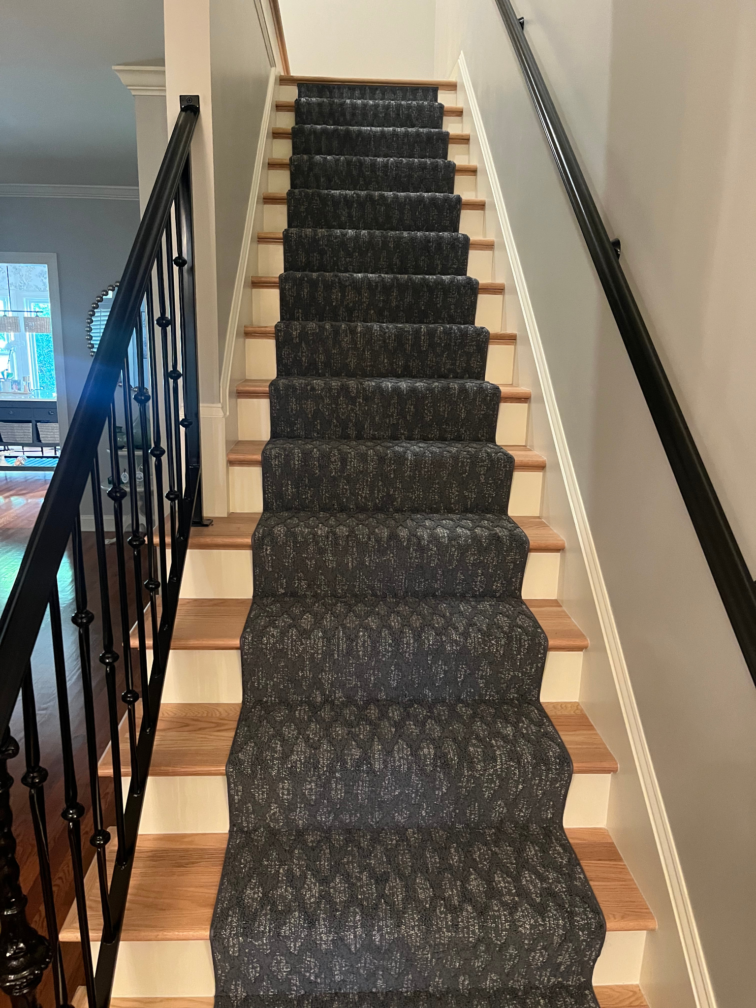 Staircase with black carpet runner and white risers, black handrails on both sides.