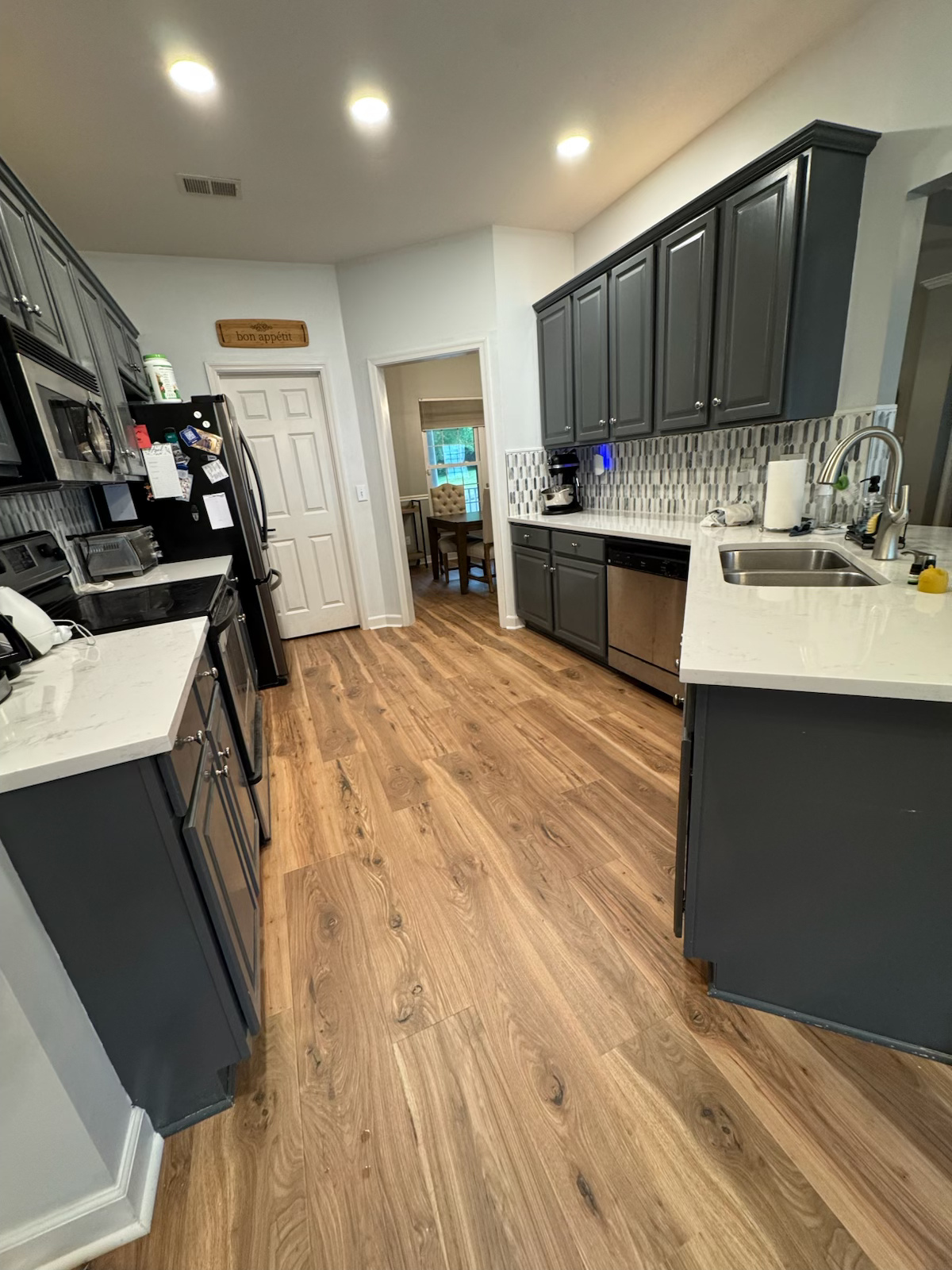 Bright modern kitchen with dark cabinets, white countertops, and wood-look flooring