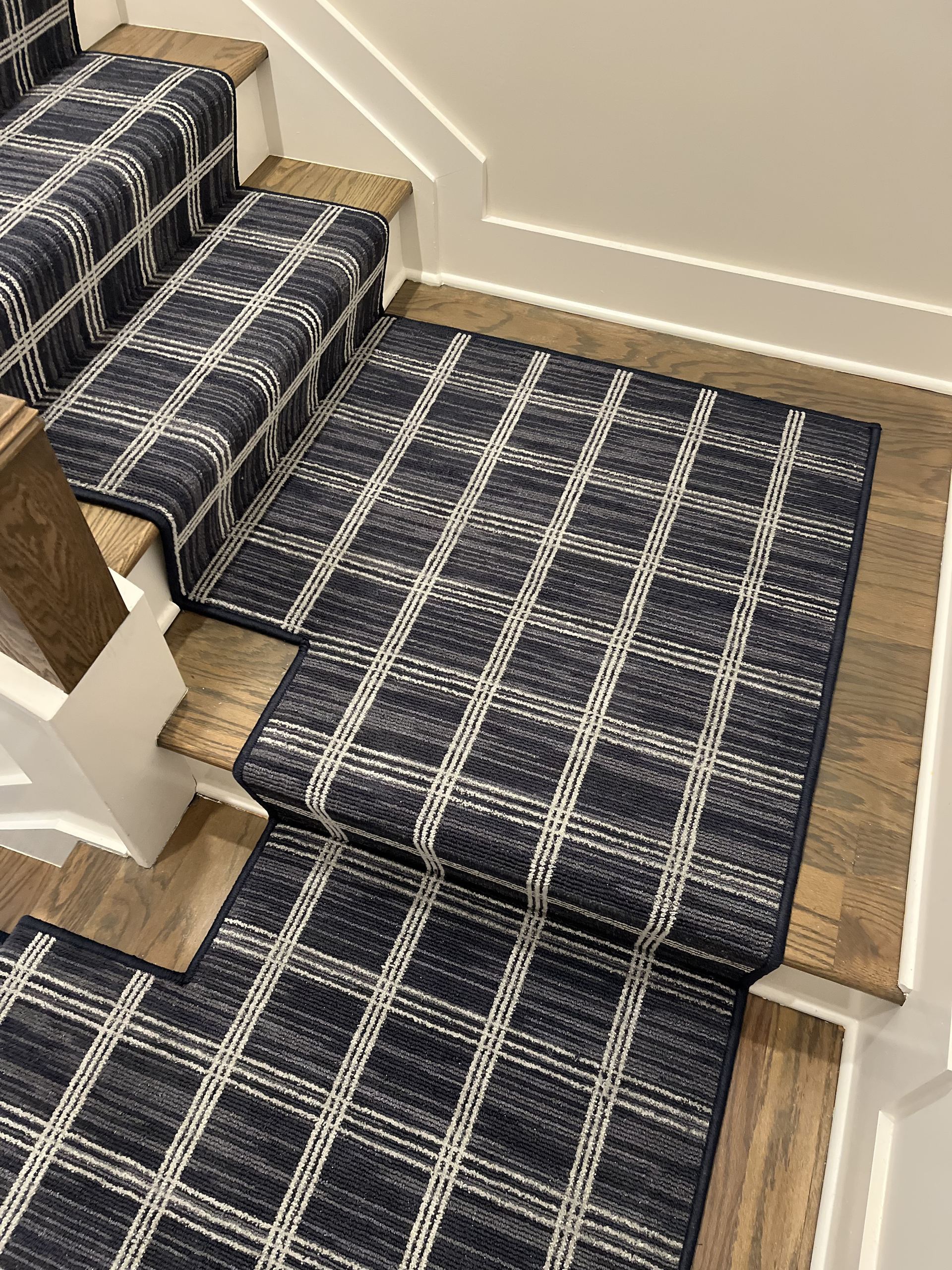 Staircase with navy plaid carpet runner and matching landing rug on wooden stairs