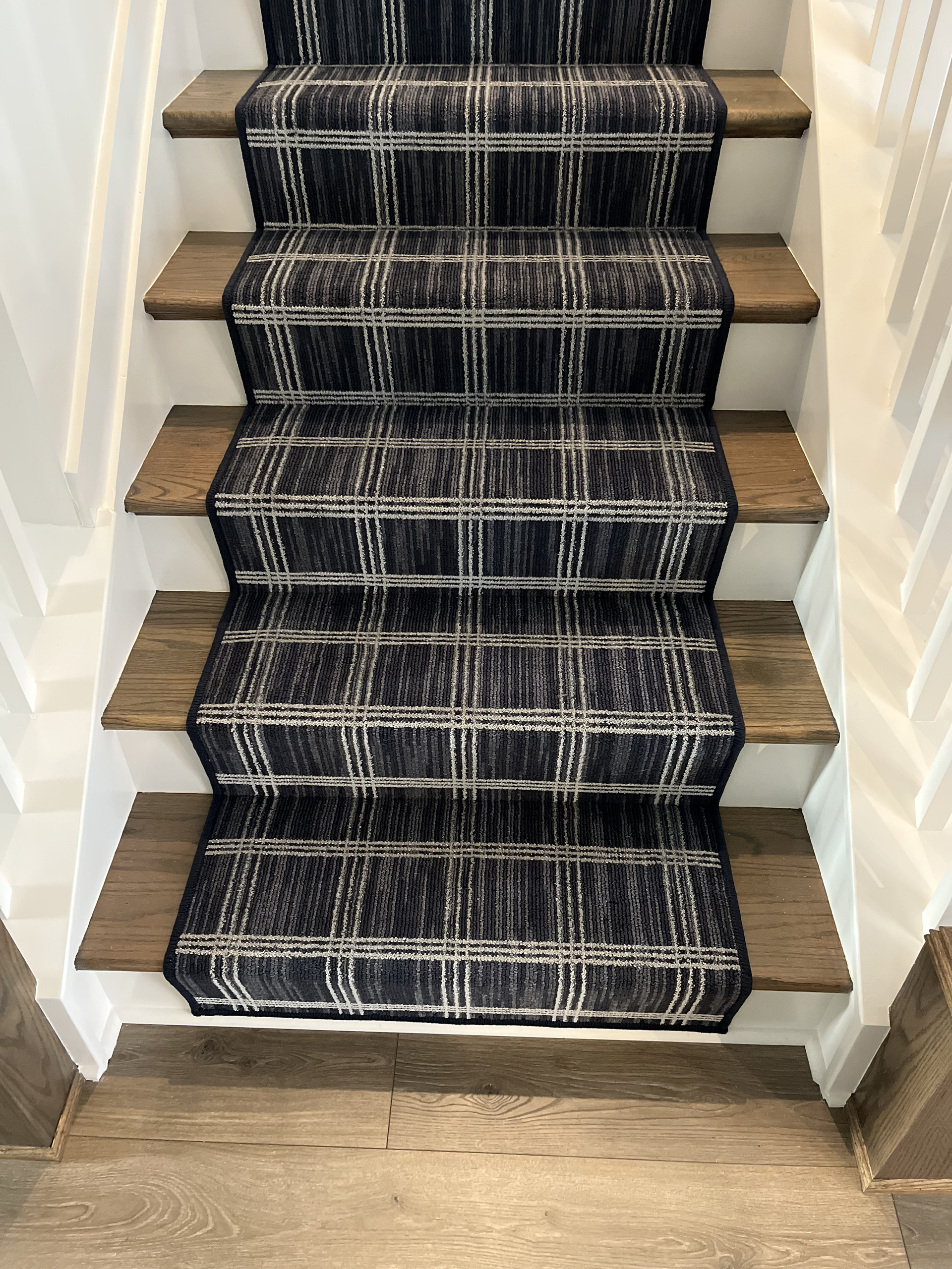 Carpeted staircase with dark patterned runner in a narrow hallway.