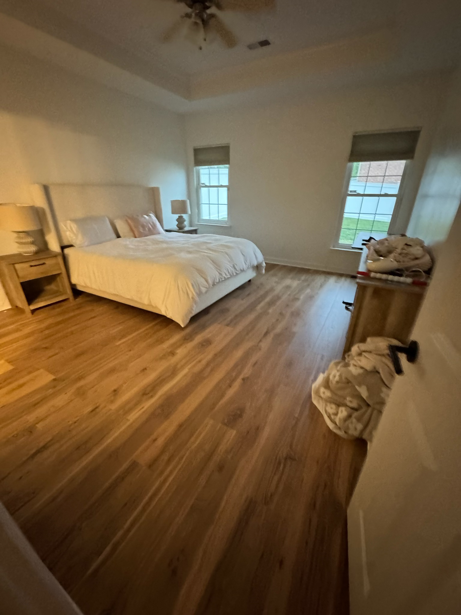 Empty bedroom with white bed, wood floors, and two windows in soft daylight