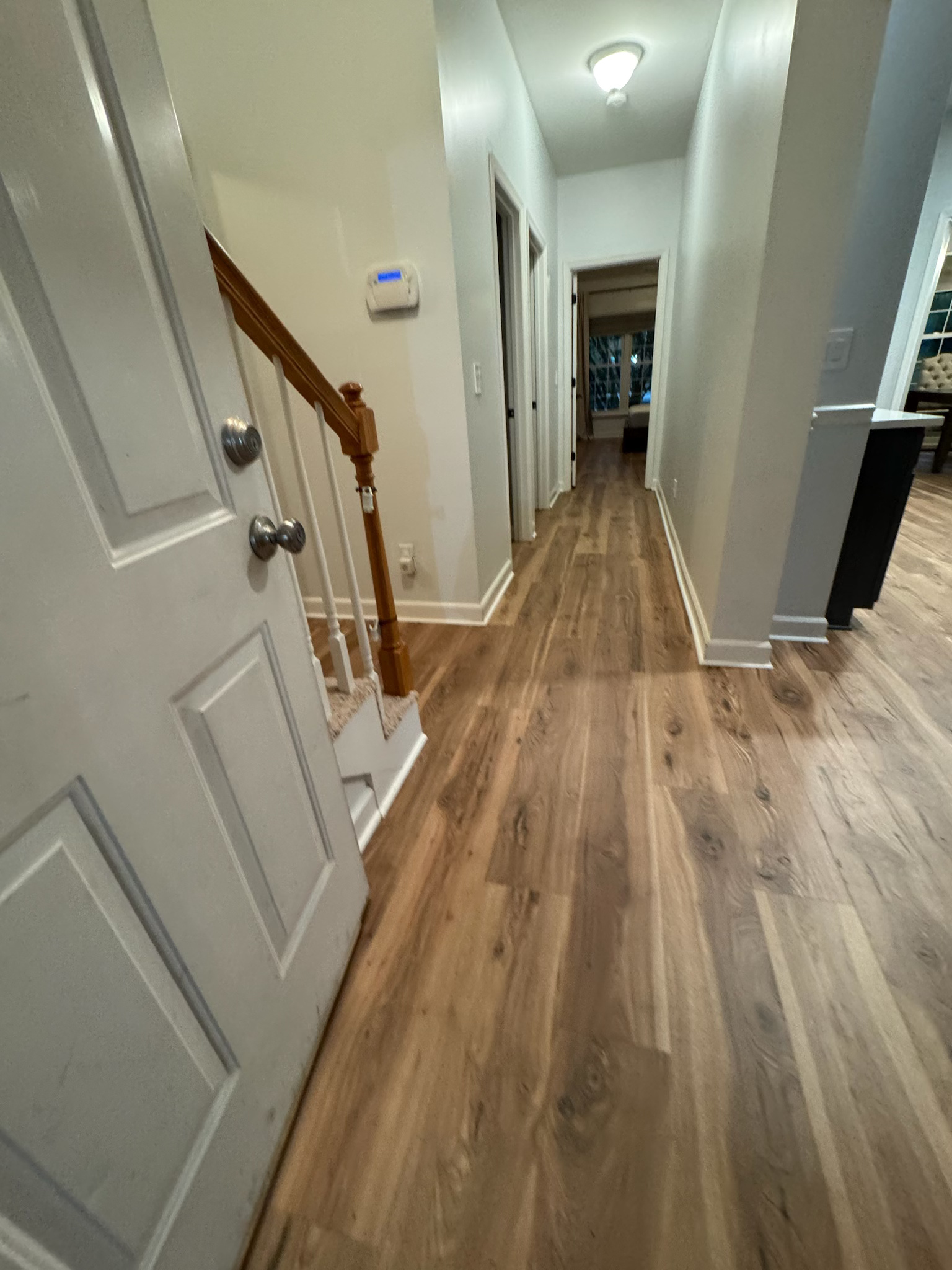 Narrow hallway with wood flooring, white walls, staircase railing, and recessed ceiling lights