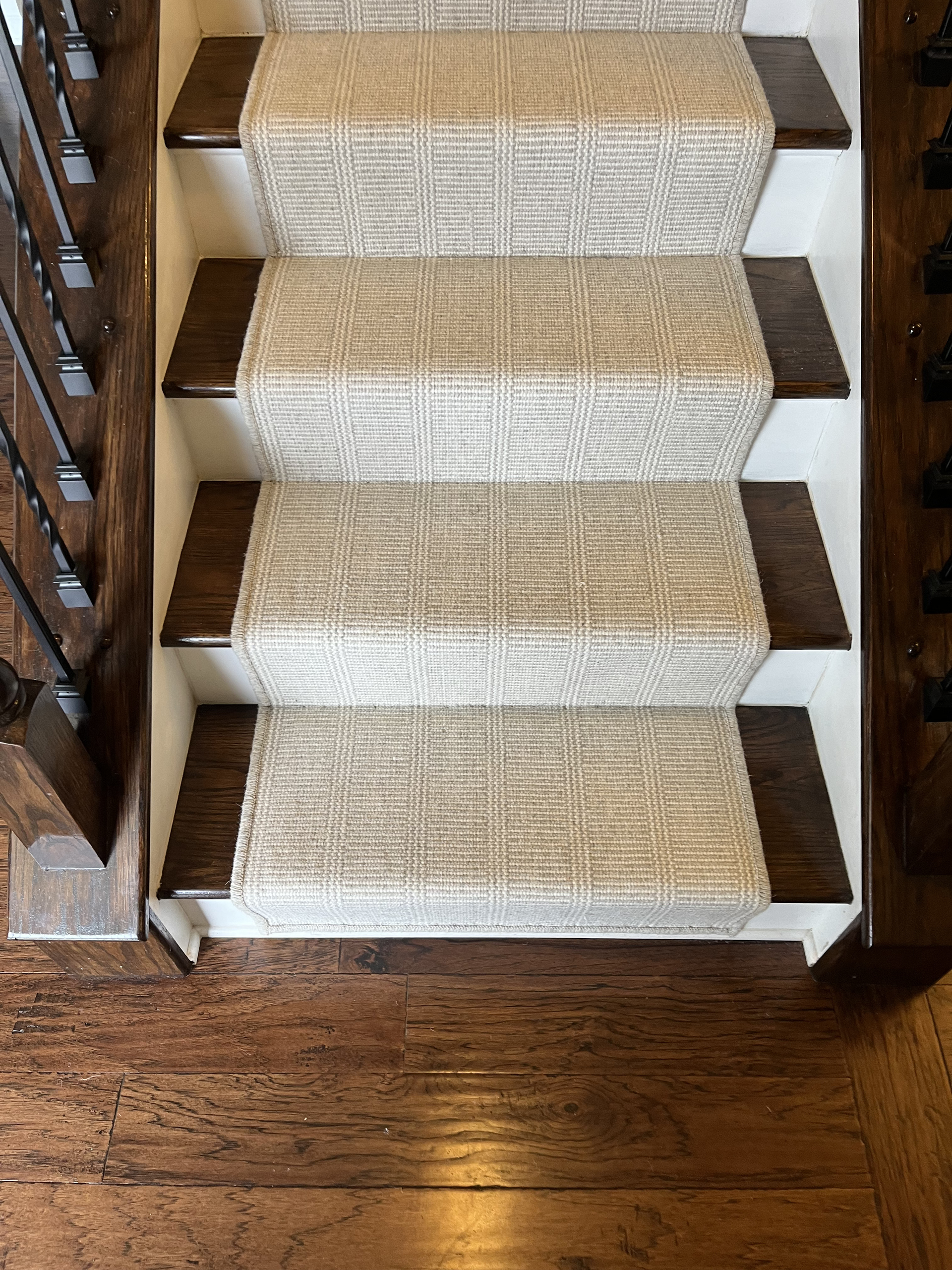 Carpeted staircase with wood side rails leading down to a hardwood floor