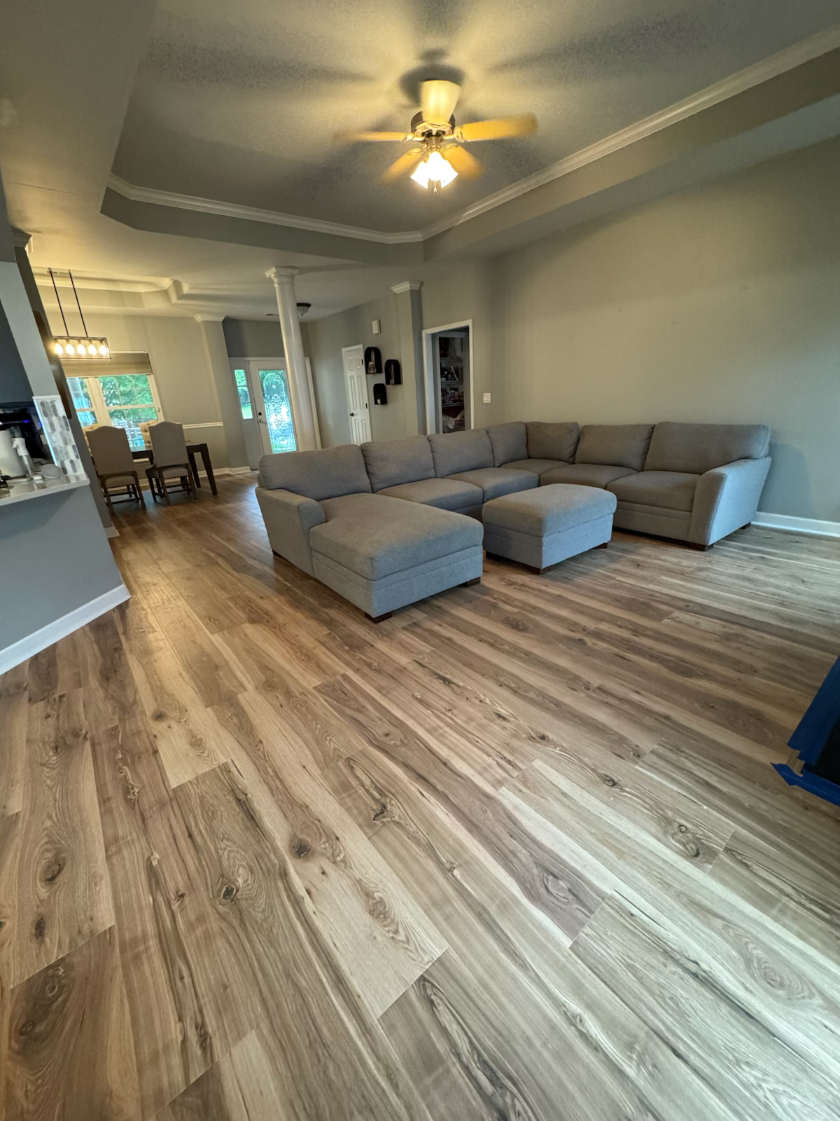 Bright living room with gray sectional sofa, wood floors, ceiling fan, and open dining area