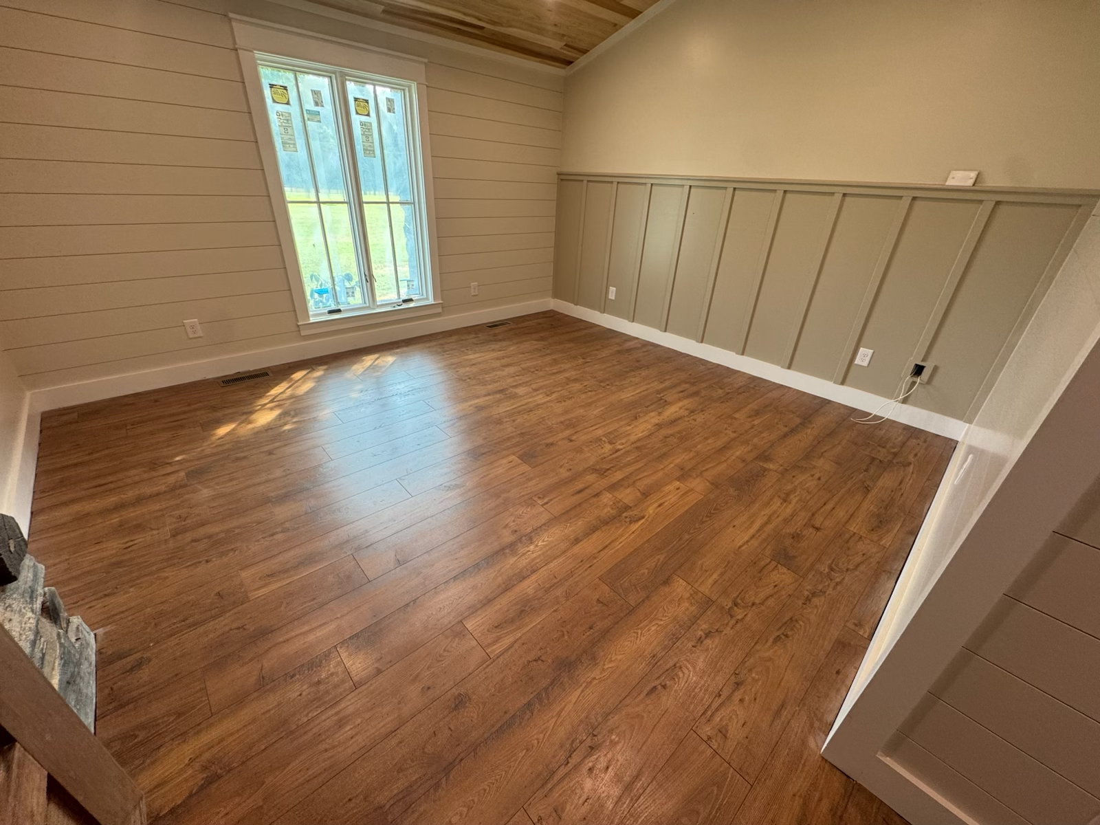 Empty room with hardwood floors, window, and paneled wall.