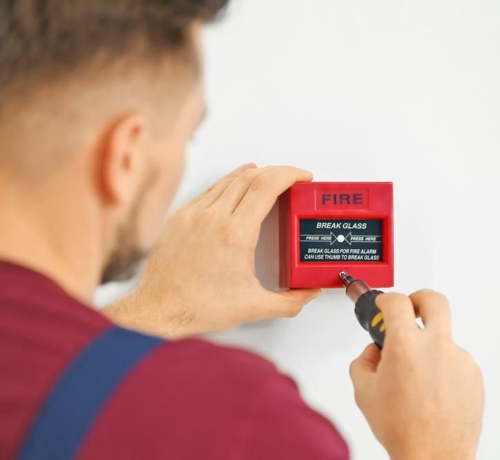 A Man Is Fixing A Fire Alarm With A Screwdriver — FNQ Smoke Alarms & Maintenance In Malanda, QLD