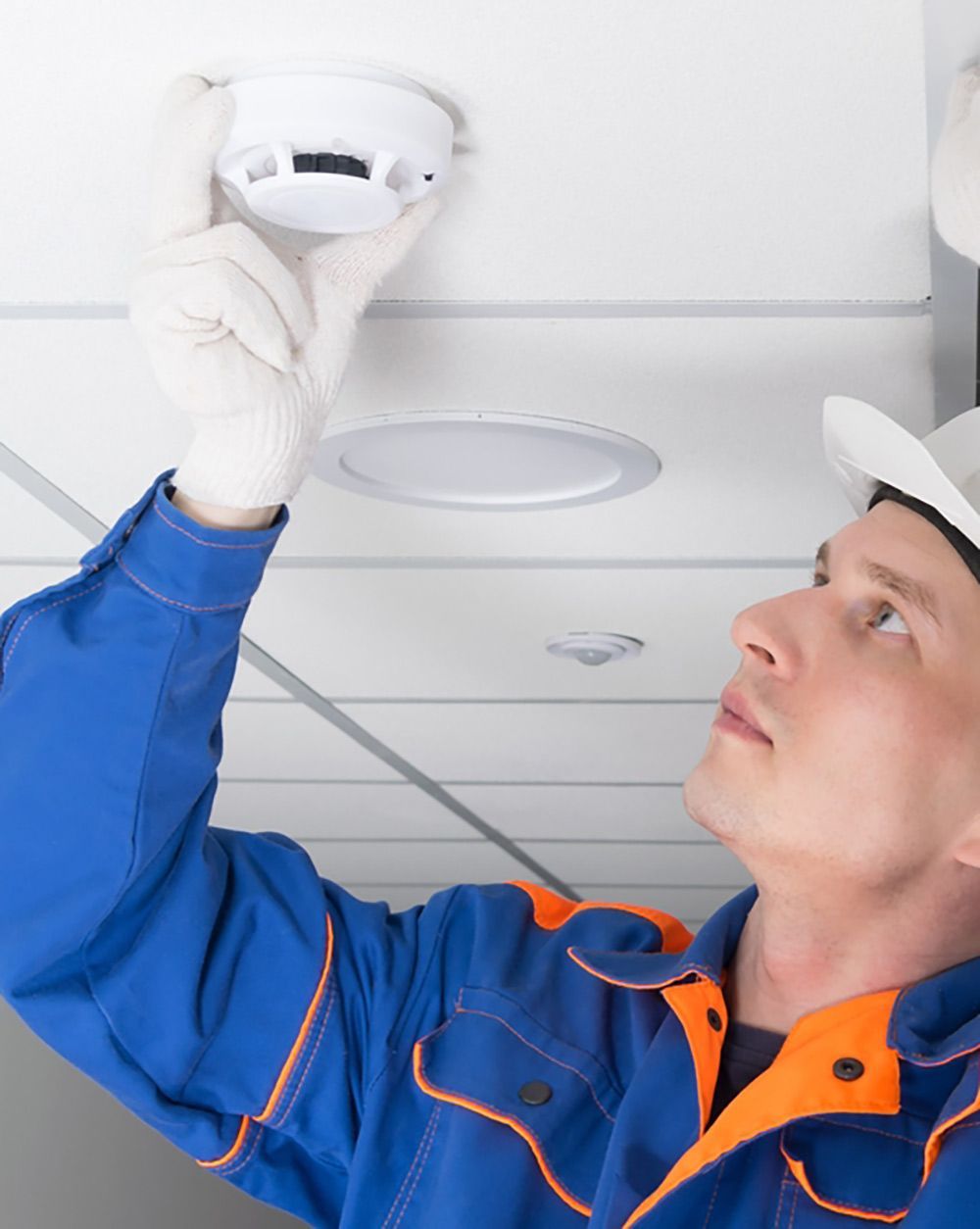 A Man Is Installing A Smoke Detector On The Ceiling — FNQ Smoke Alarms & Maintenance In Innisfail, QLD