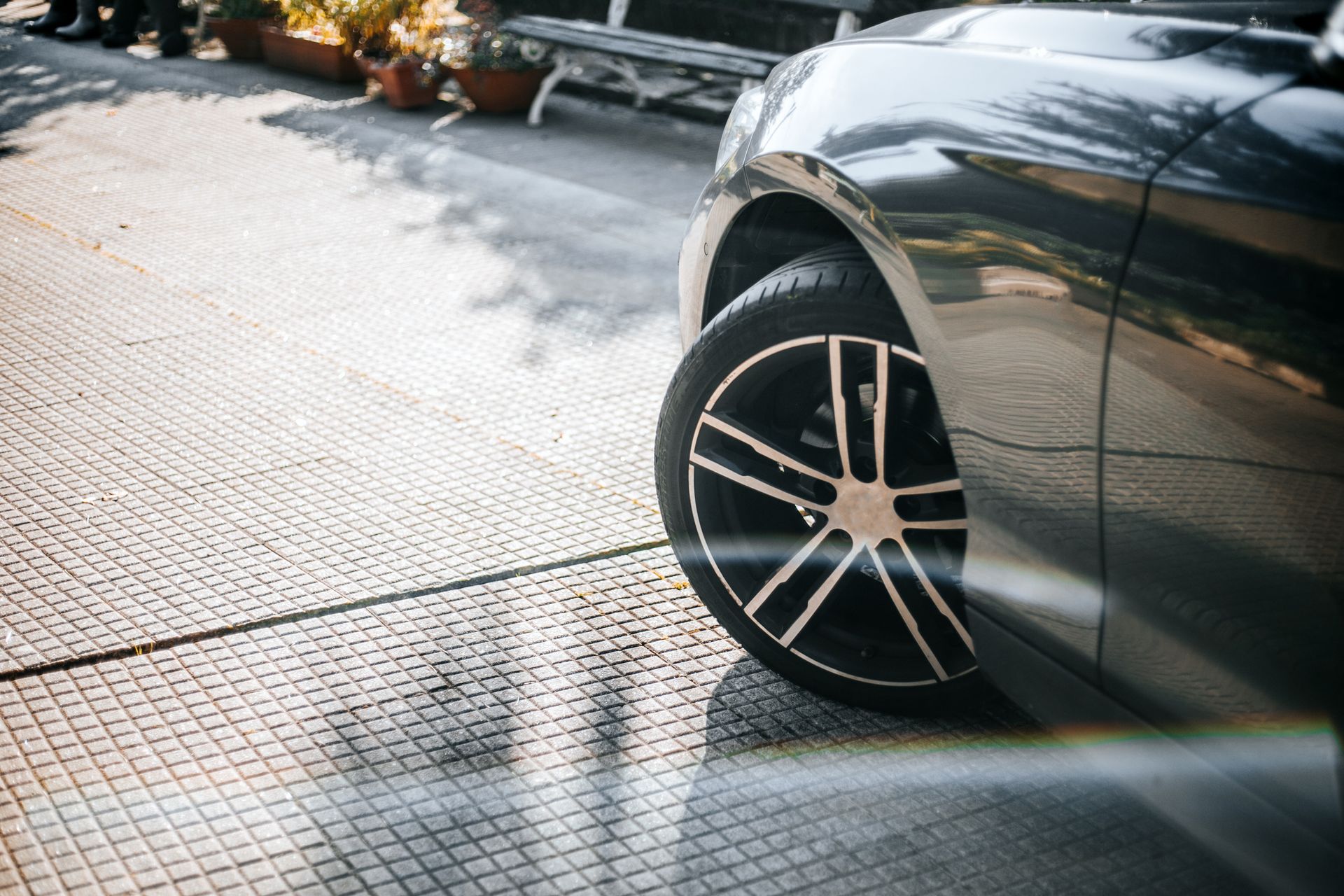 Close-up of car front wheel on tiled driveway with plants in background.