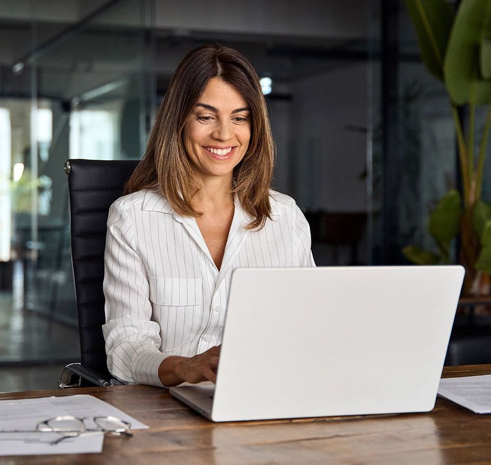 A woman is sitting at a desk using a laptop computer.