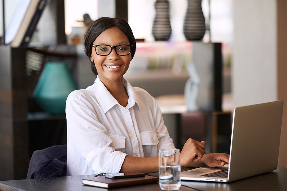 A woman is sitting at a table with a laptop and a glass of water.