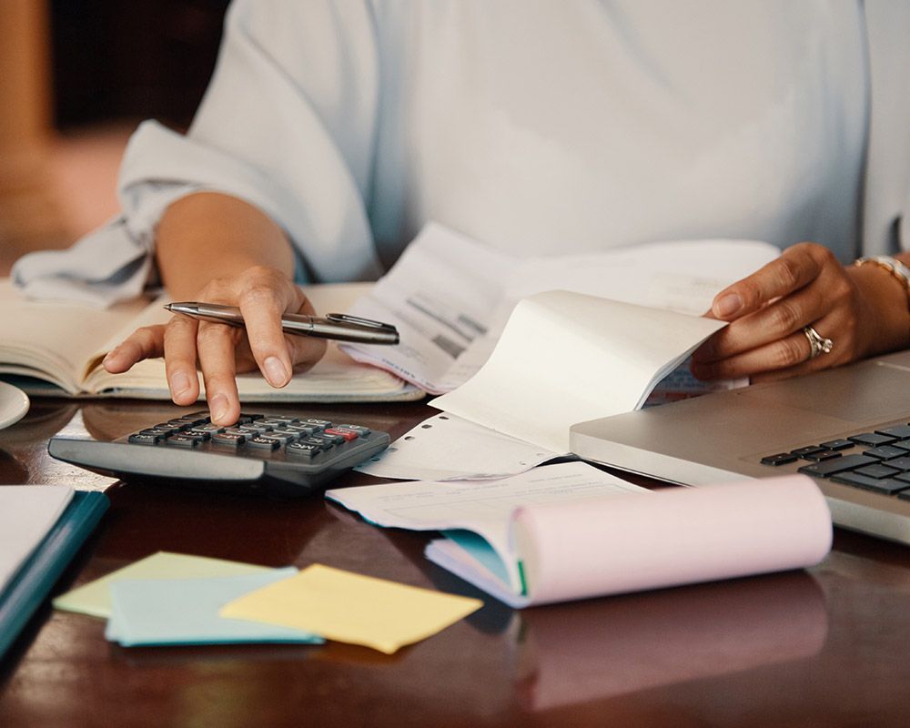 A woman is sitting at a desk using a calculator and a pen.