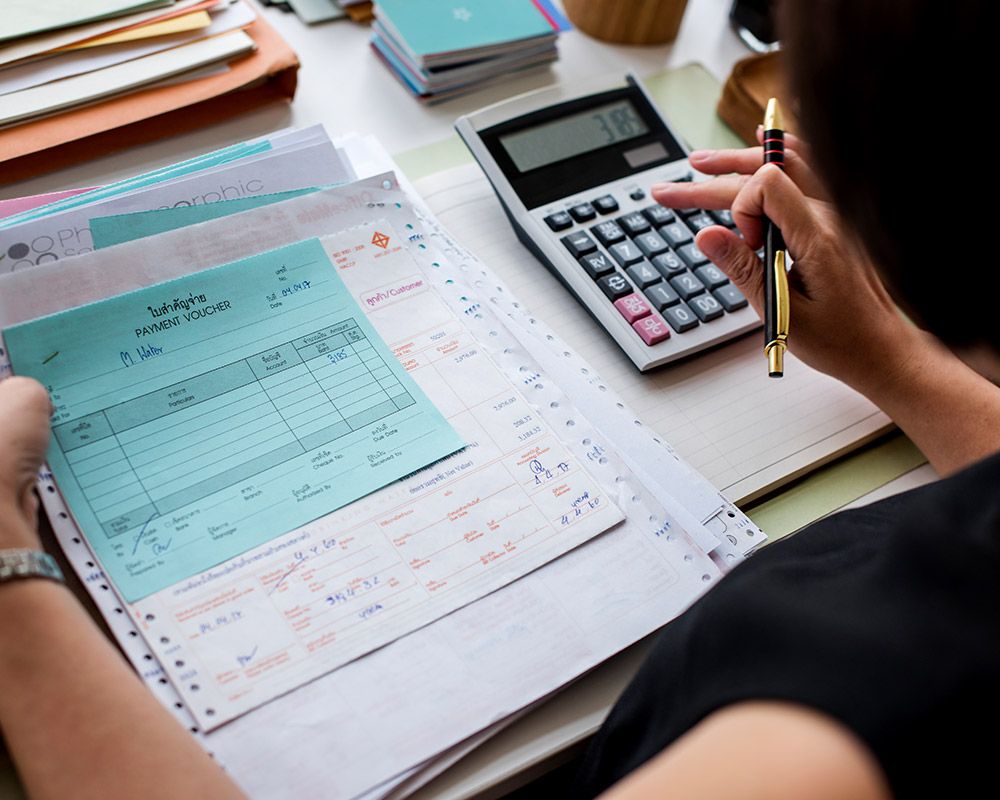 A woman is sitting at a desk using a calculator and a pen.