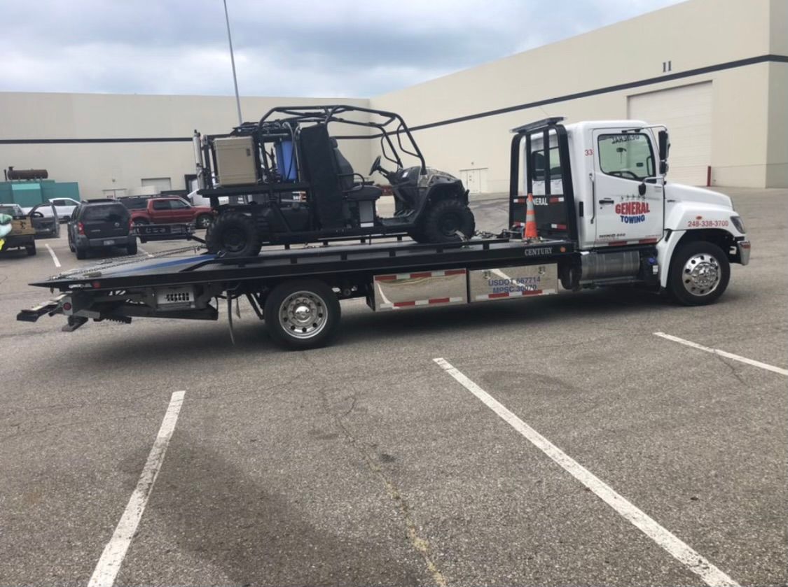 A tow truck transports a black ATV on its flatbed in a parking lot.