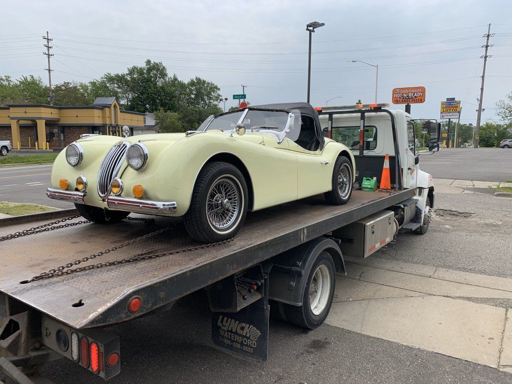 Yellow vintage Jaguar roadster on a tow truck, likely being transported.