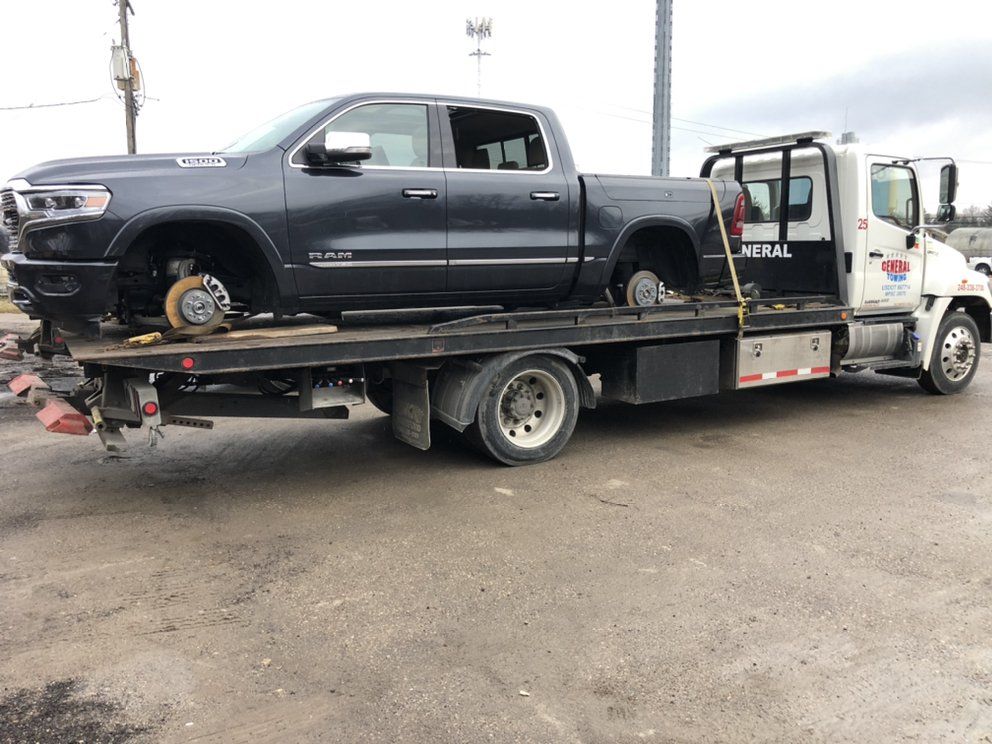 Dark gray Ram pickup truck on a tow truck, missing its front and rear wheels.