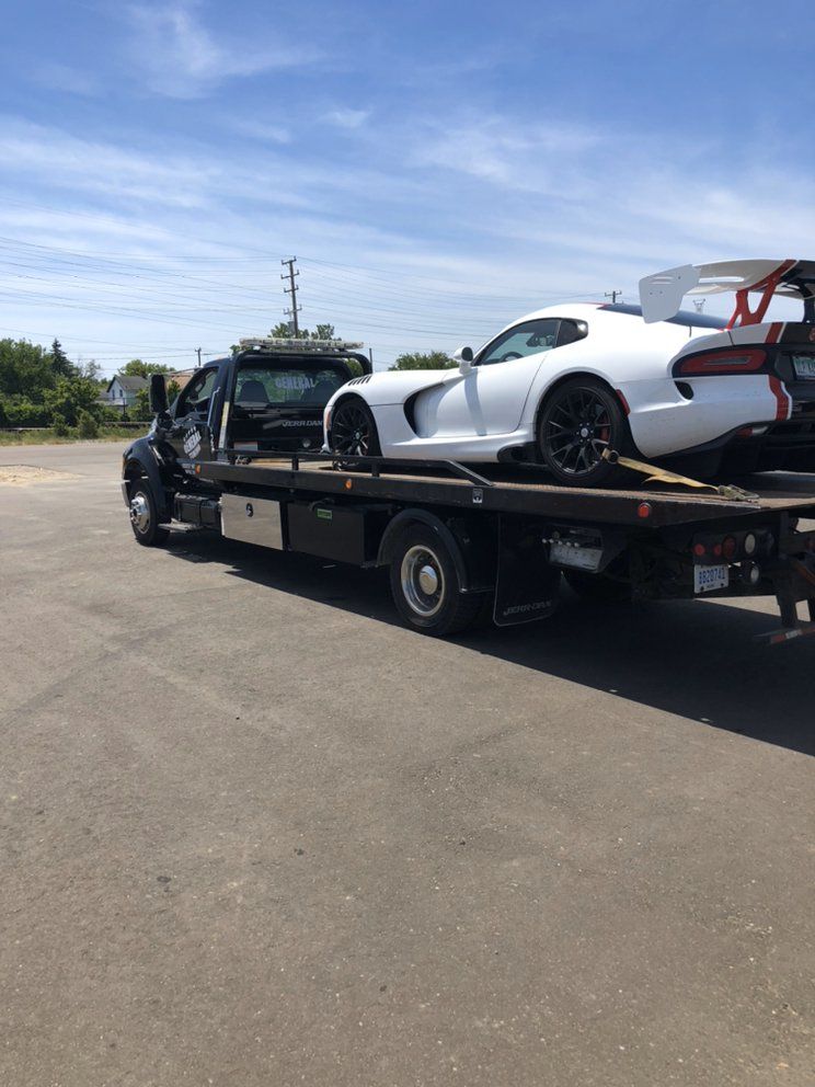 White Dodge Viper sports car being transported on a flatbed tow truck under a blue sky.