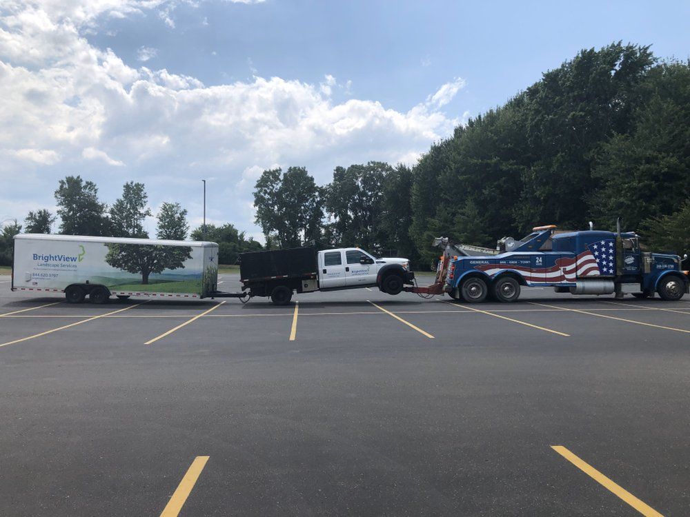 A tow truck towing a truck and trailer in a parking lot on a sunny day.