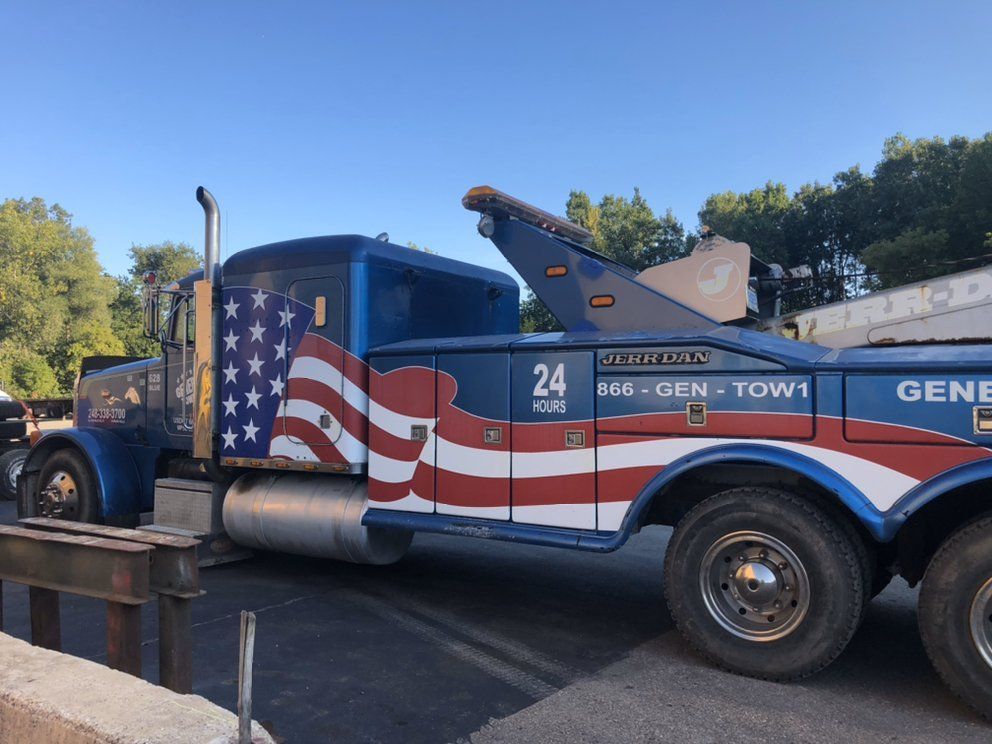 Blue tow truck with American flag design parked outdoors.