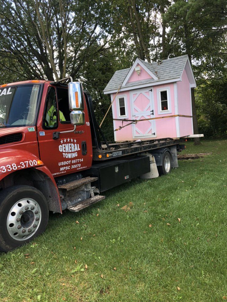 Pink playhouse on a tow truck. The truck is red, parked on grass.