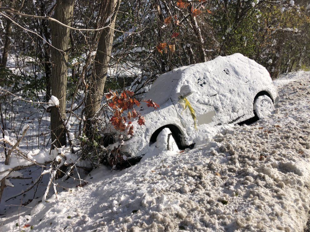 A snow-covered car stuck off the road in a snowy ditch, near trees.