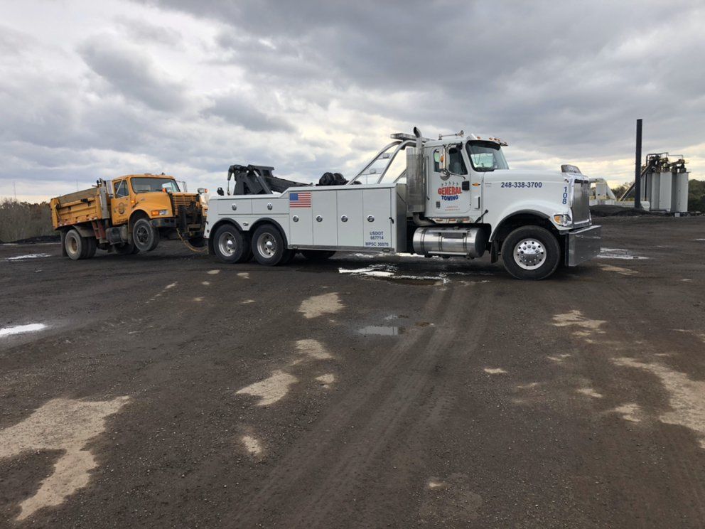 Tow truck towing a yellow dump truck on a cloudy day.