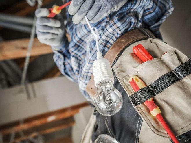 An electrician is working on a light bulb with a screwdriver.