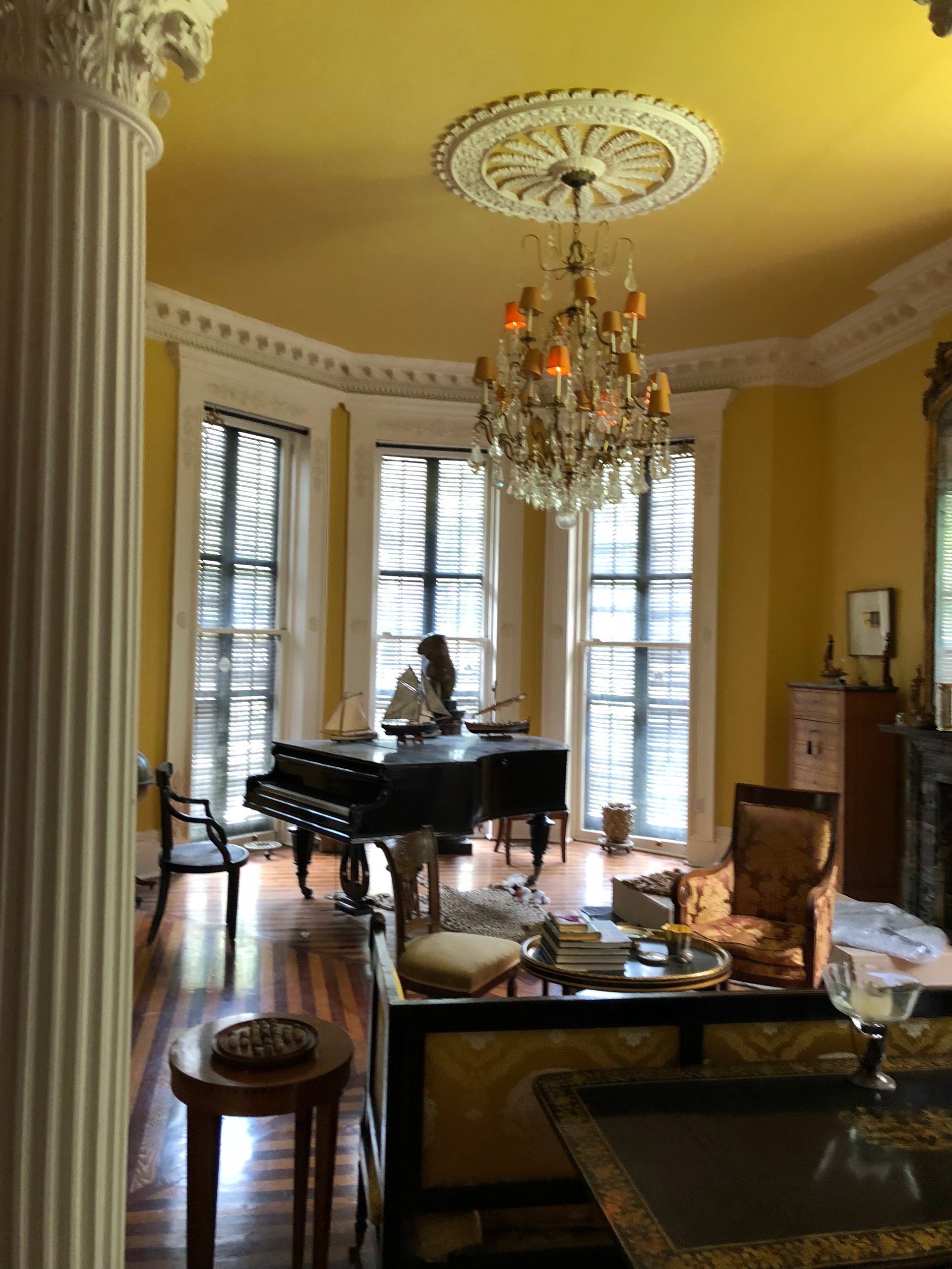 A woman is sitting at a piano in a living room with a chandelier hanging from the ceiling.