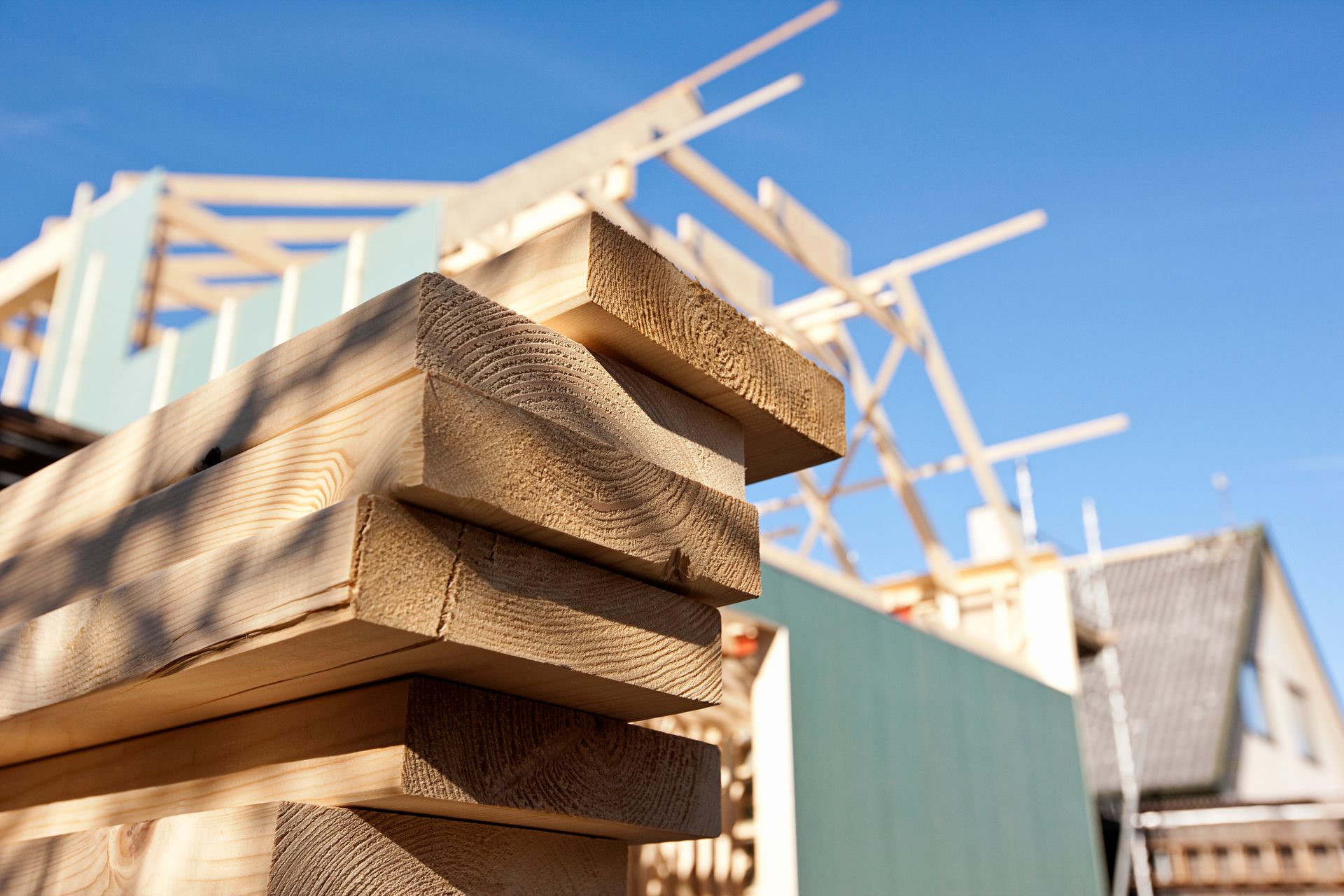 Close-up of stacked wood on site with a construction frame in the background.