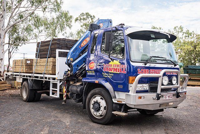 A blue truck with a crane on the back is parked in a parking lot.