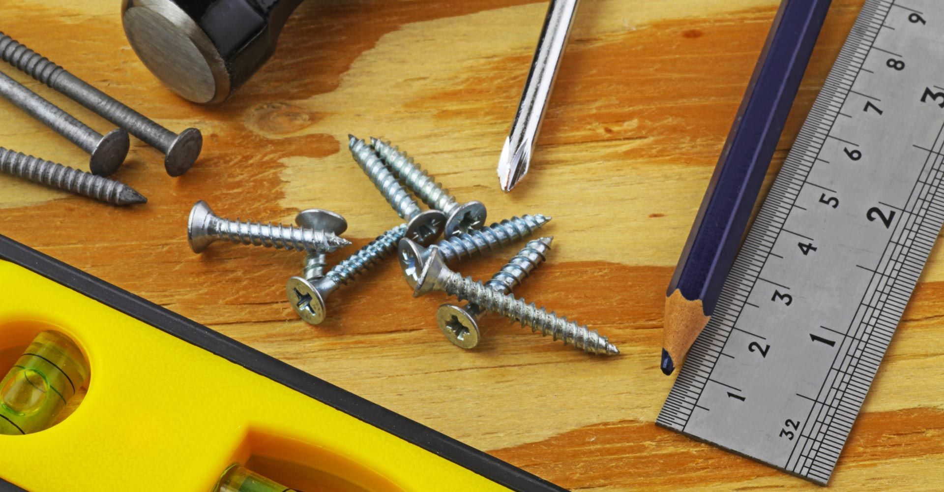 A wooden table with a ruler screws a hammer and a pencil