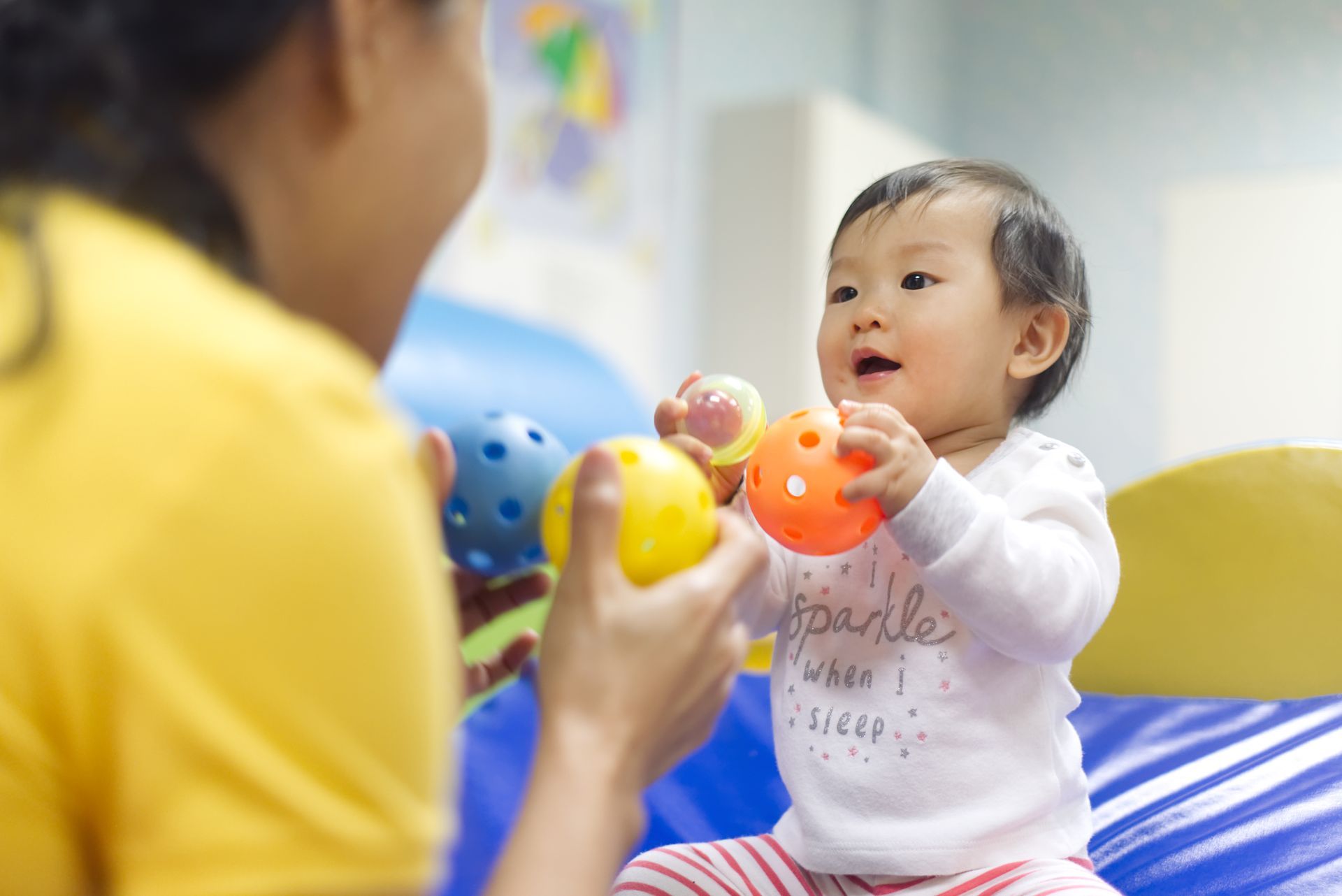 A woman is playing with a baby who is holding balls.