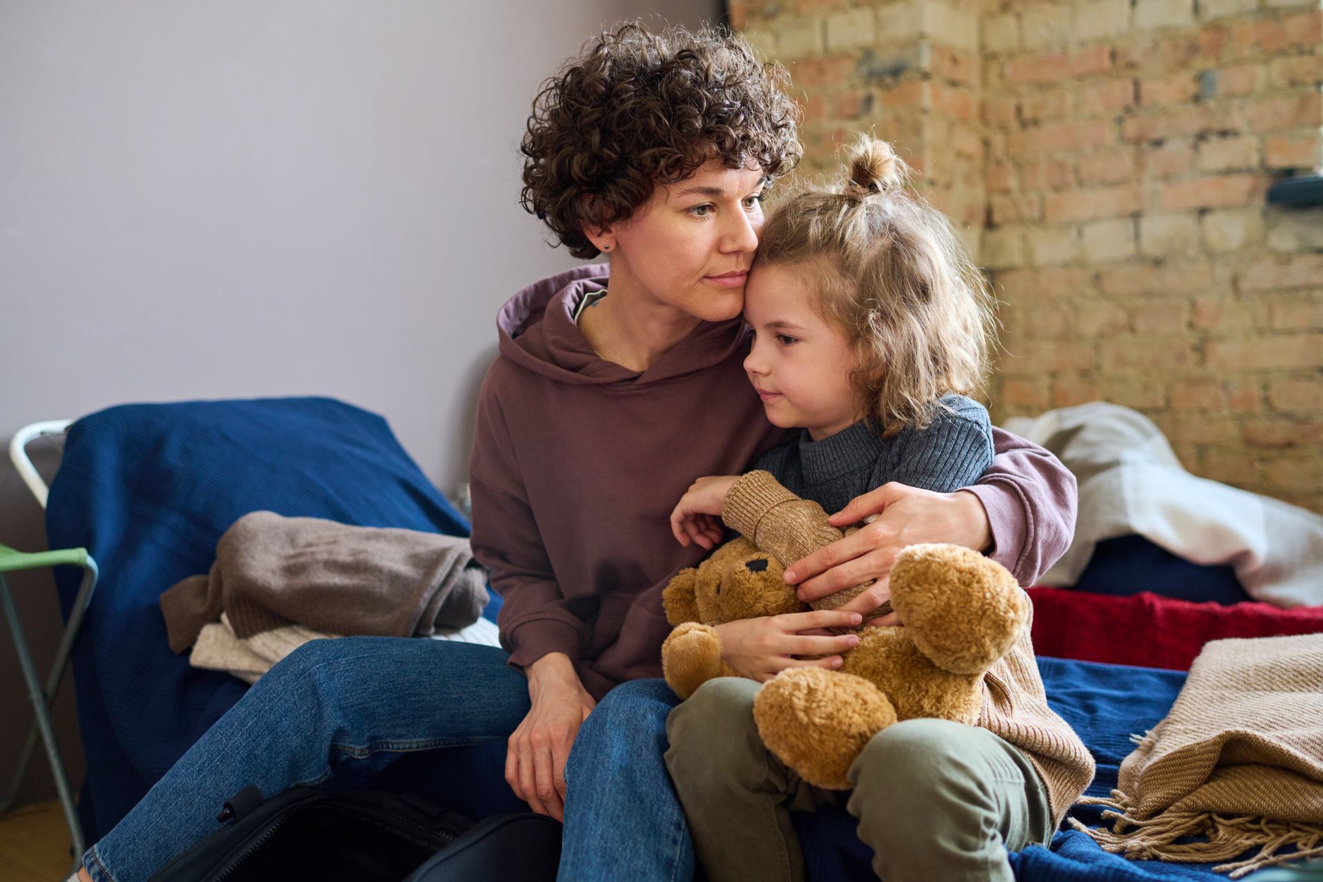 A woman is sitting on a bed with a little girl holding a teddy bear.