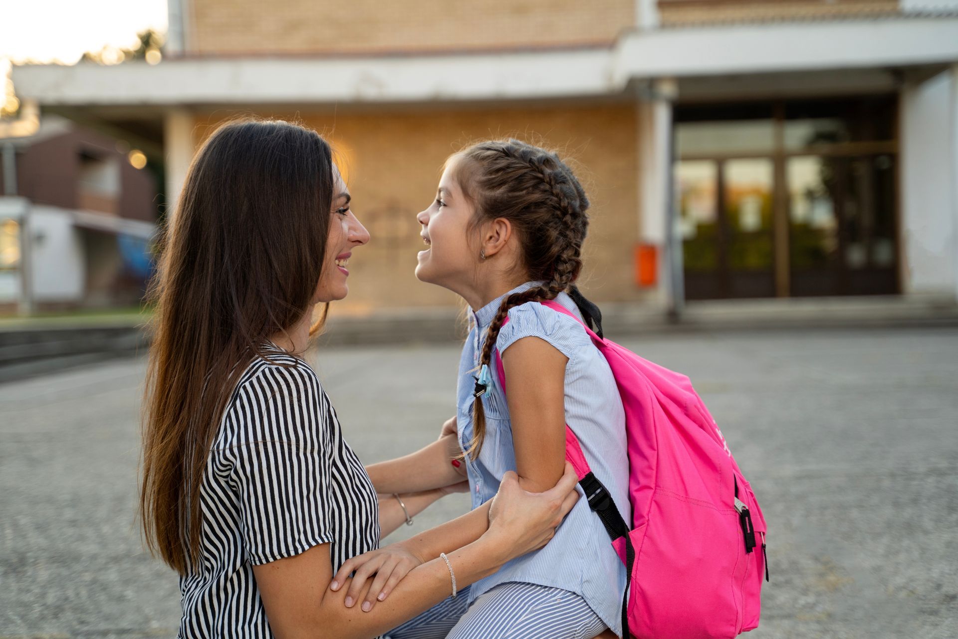 A mother and daughter are looking at each other in front of a school building.