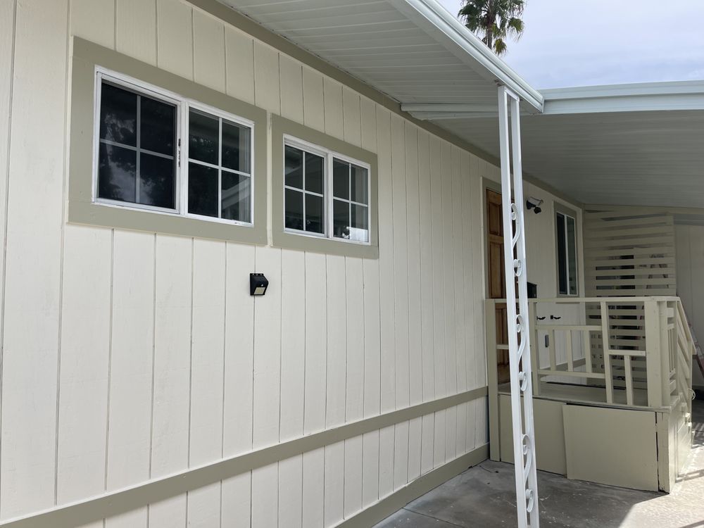 Beige mobile home exterior with windows, awning, and entryway.