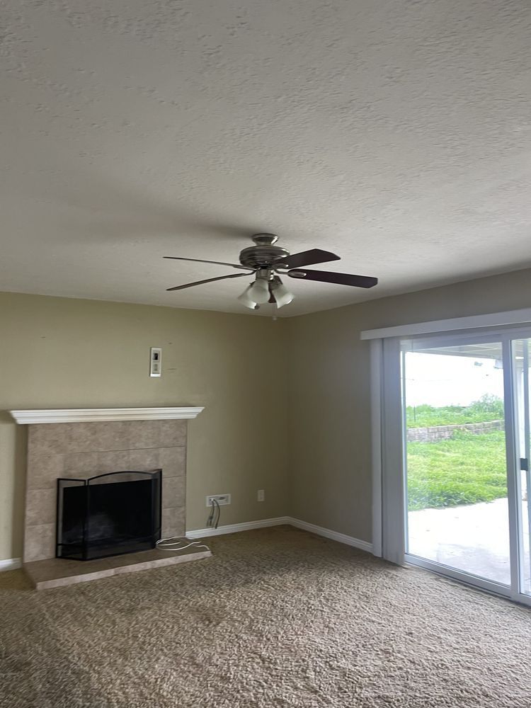 Living room with fireplace, ceiling fan, sliding glass door, and tan walls.