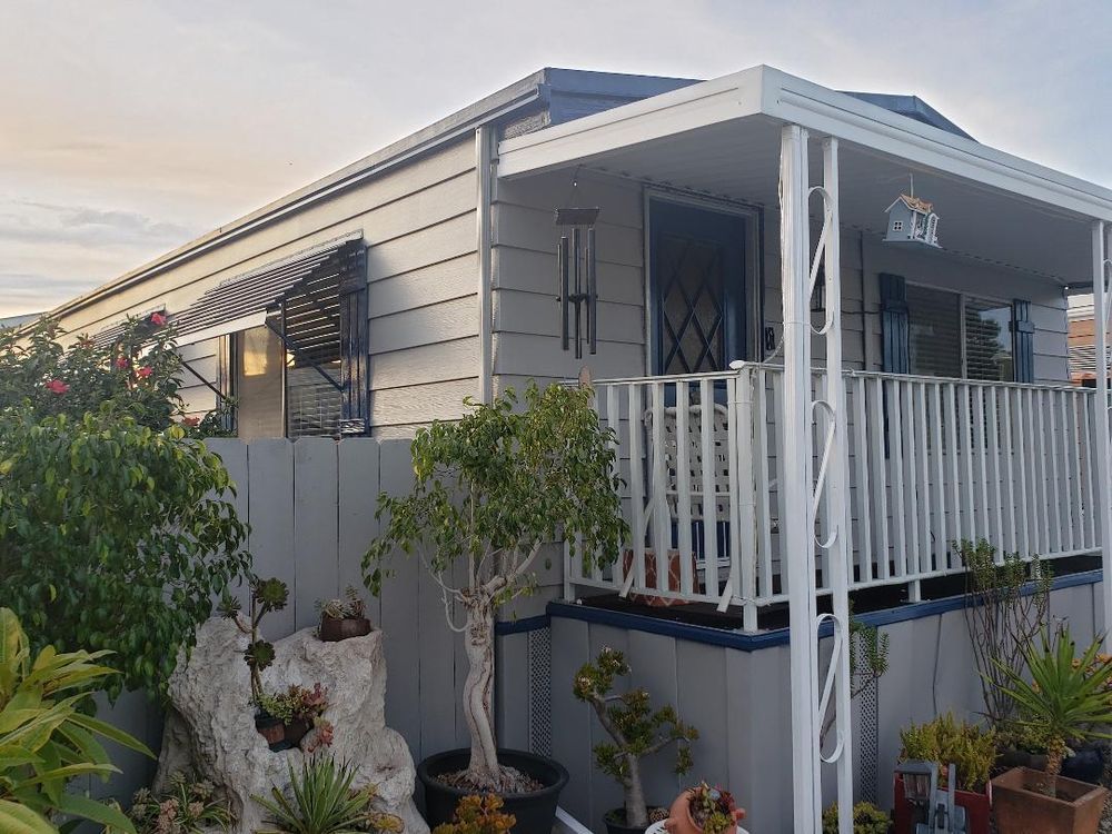 Gray mobile home with a small porch, plants, and a rock garden.