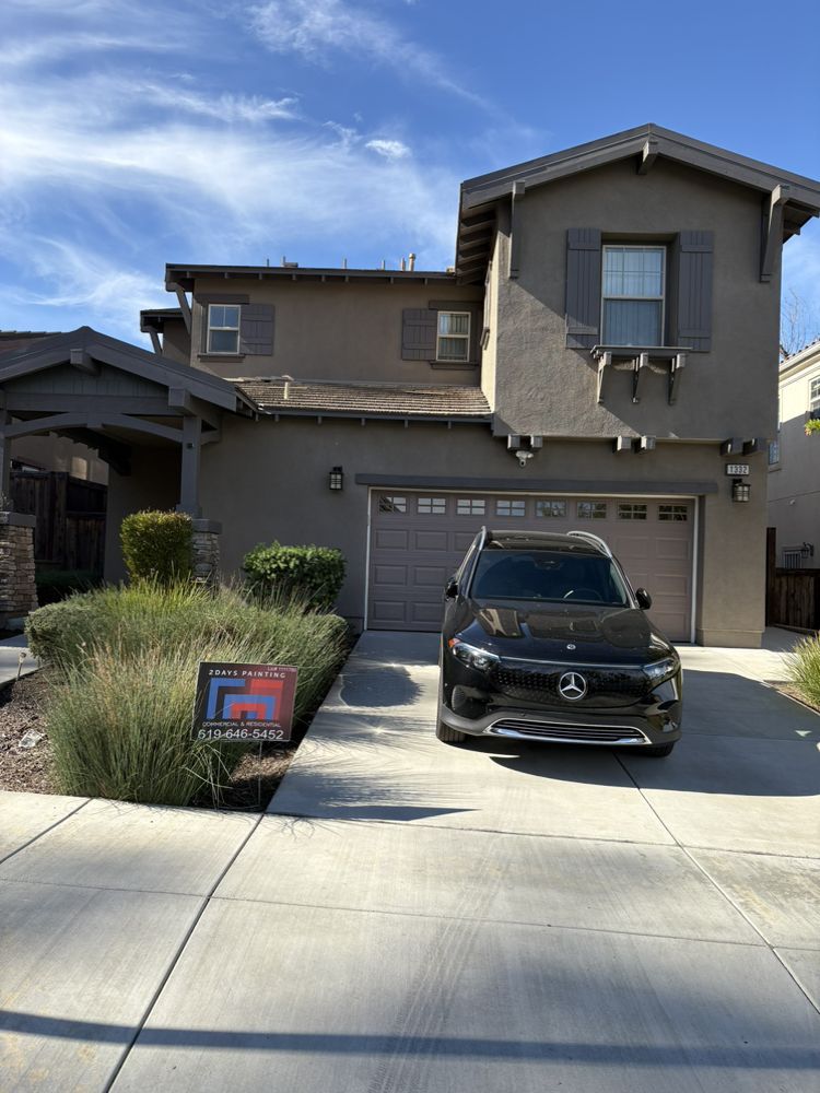 Dark SUV parked in front of a two-story beige house with a driveway. Blue sky overhead.