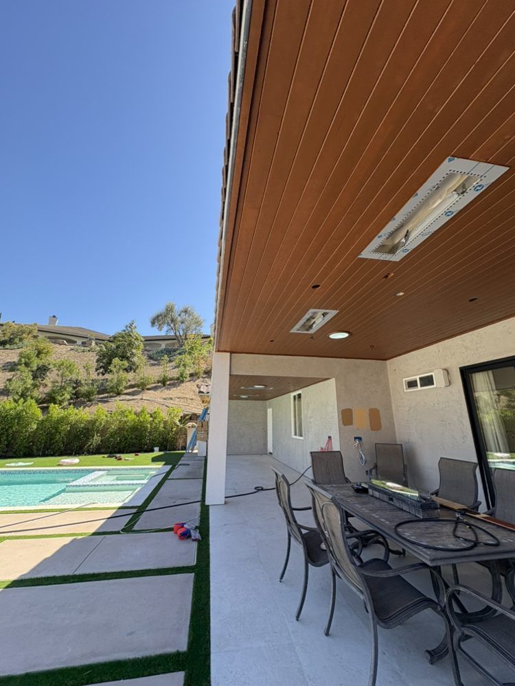 Patio with a pool, outdoor dining table, and brown wood ceiling under a blue sky.