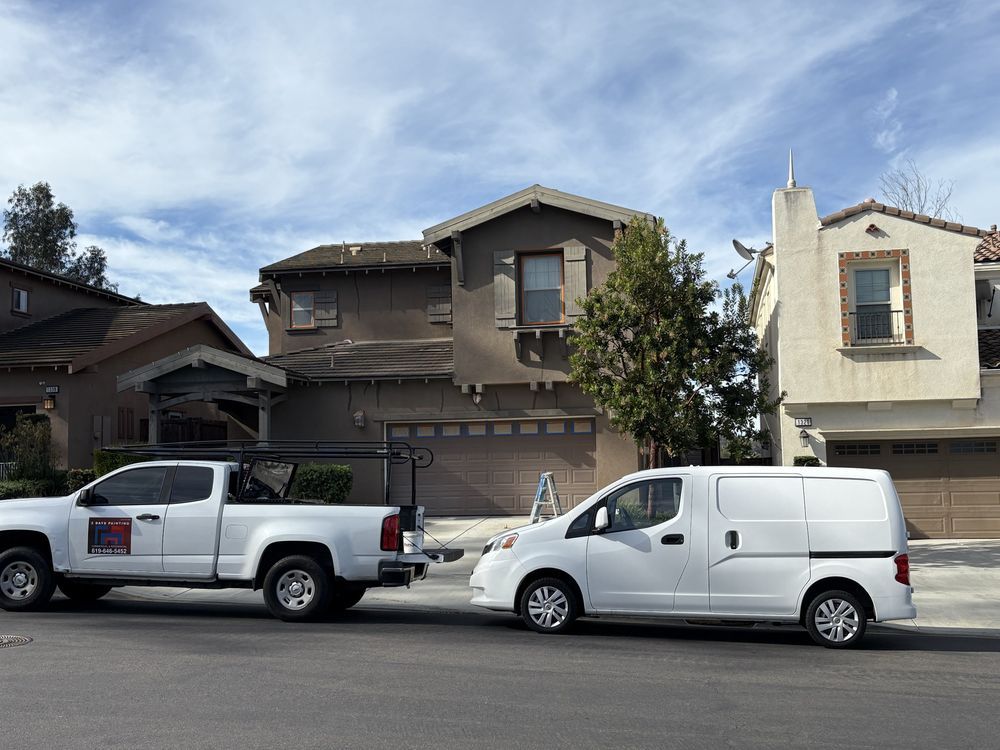 White pickup truck and van parked in front of two-story houses on a street with a cloudy sky.