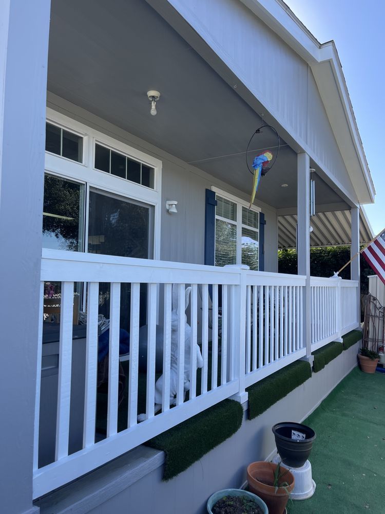 A light gray house with a white porch railing and awning. A parrot decoration hangs near the windows.