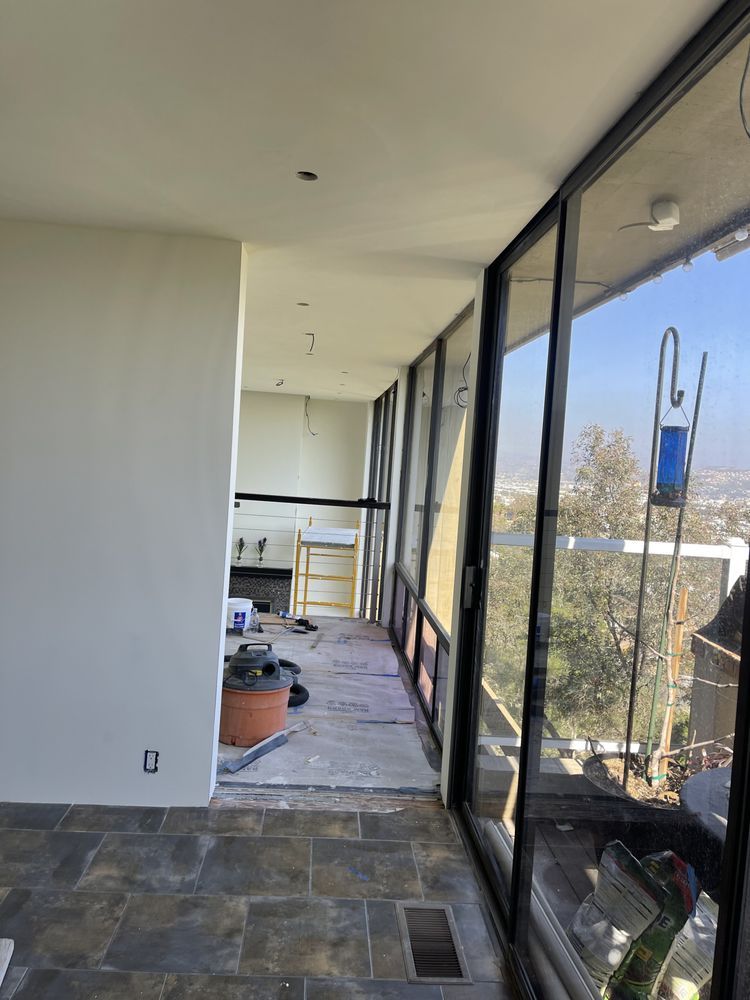 Interior construction: hallway with large windows, unfinished flooring, and visible landscape.