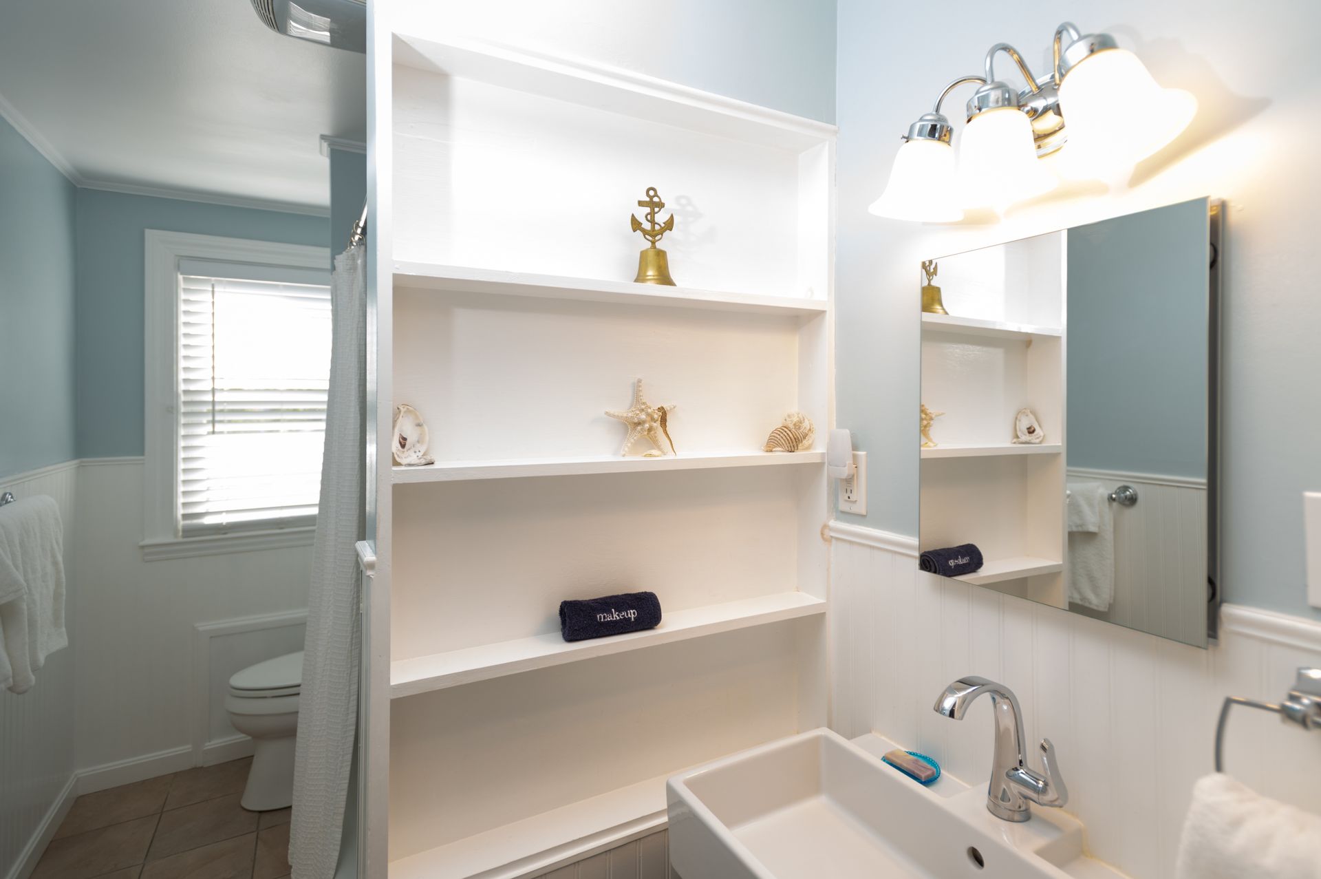 Bathroom with white shelves displaying nautical decor, blue walls, a sink, and a mirror.