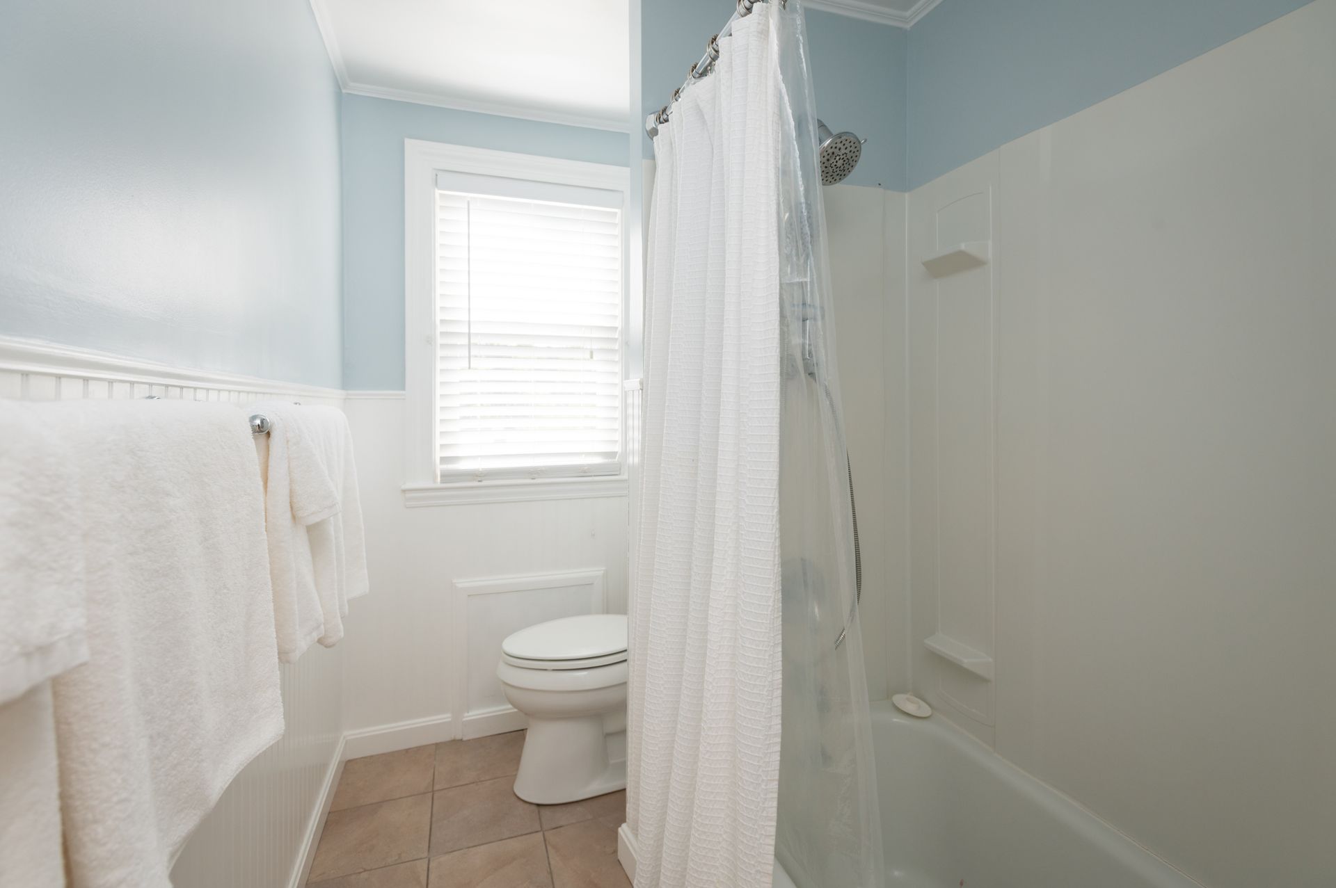Bathroom with blue and white walls, shower with a curtain, window with blinds, and a toilet.
