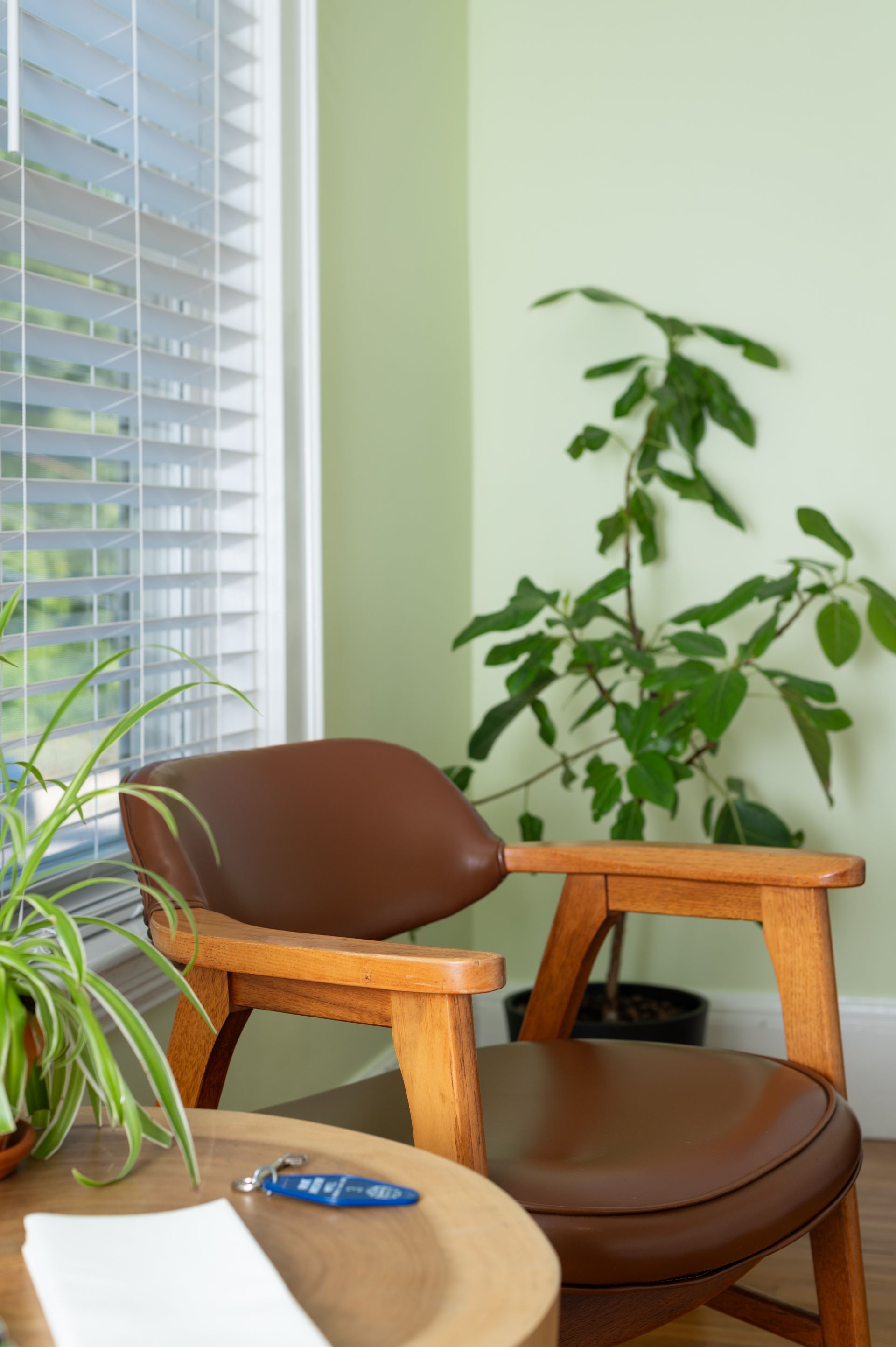 Brown leather chair beside a window with blinds, a plant, and a small wooden table.