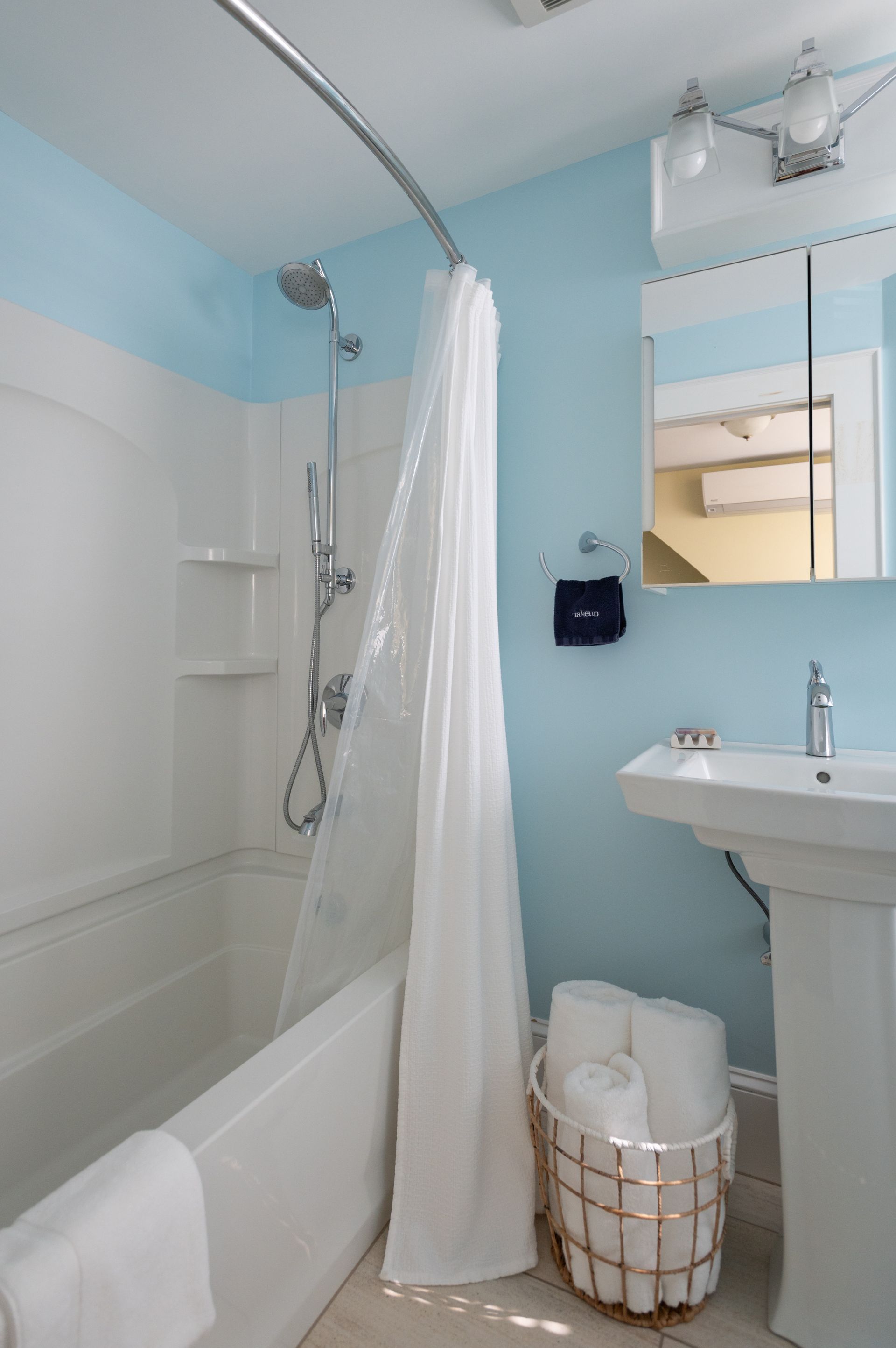 Bathroom with a white bathtub, blue walls, a sink, and rolled towels in a basket.